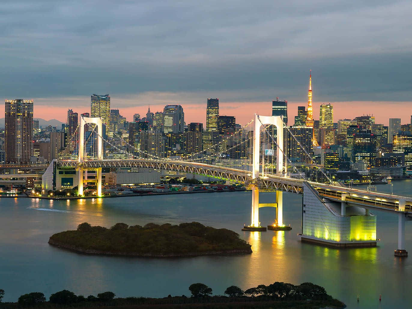 Rainbow Bridge 桌布 壁紙 — 彩虹橋在黃昏時分在東京灣上閃耀金光，城市燈光倒映在水面上，遠處的東京塔閃閃發光。