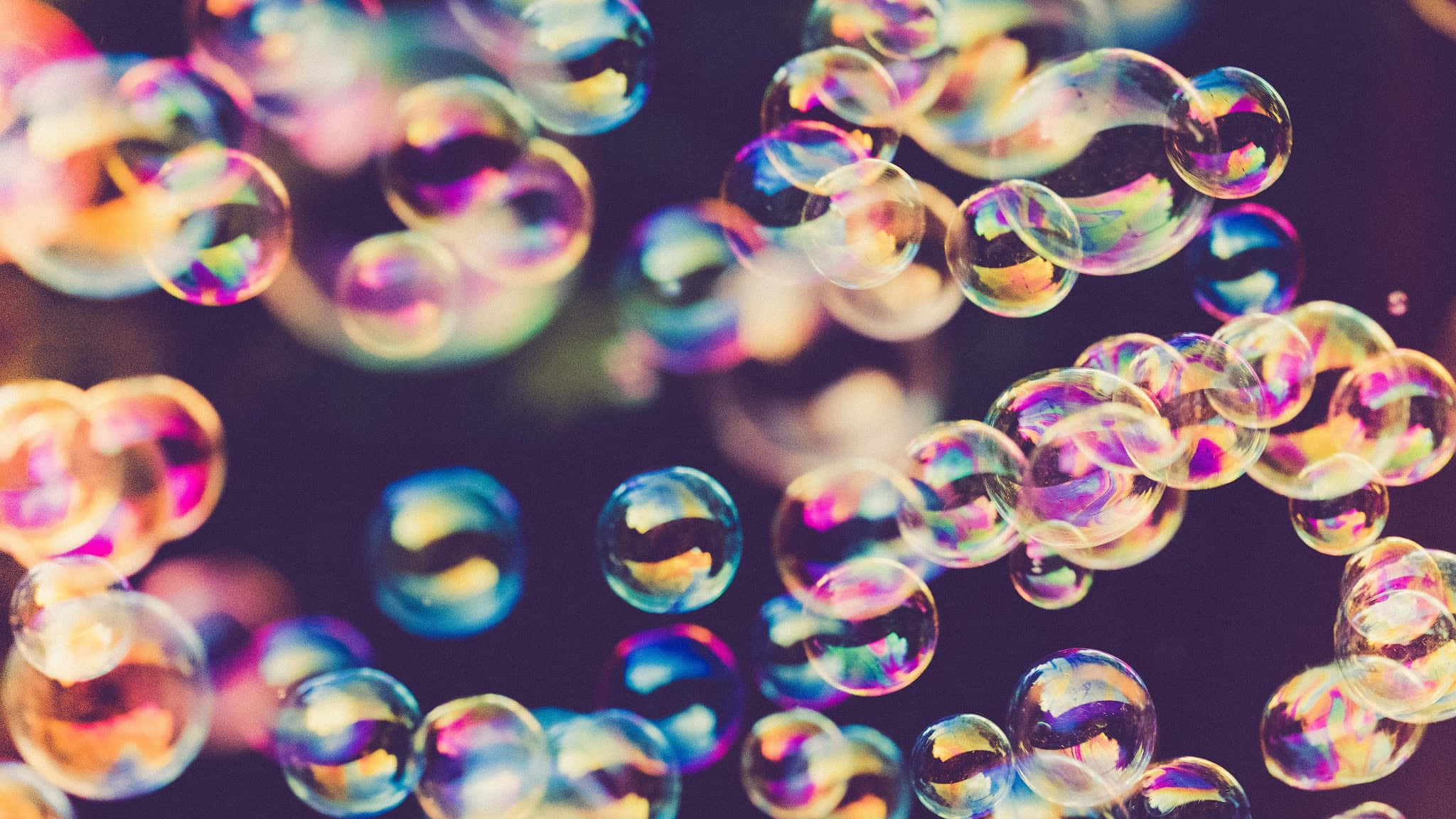 復古 桌布 壁紙 — 彩虹色的肥皂泡在黑暗模糊的背景上漂浮並閃爍著彩虹色調。