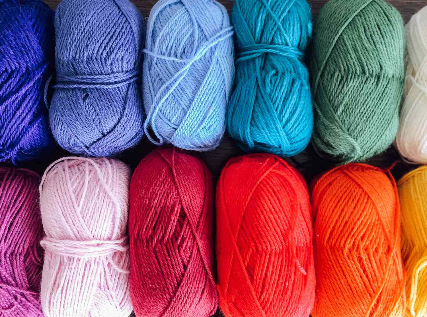 Knitting 桌布 壁紙 — 彩虹色調的鮮豔毛線球整齊排列在深色木質表面上。
