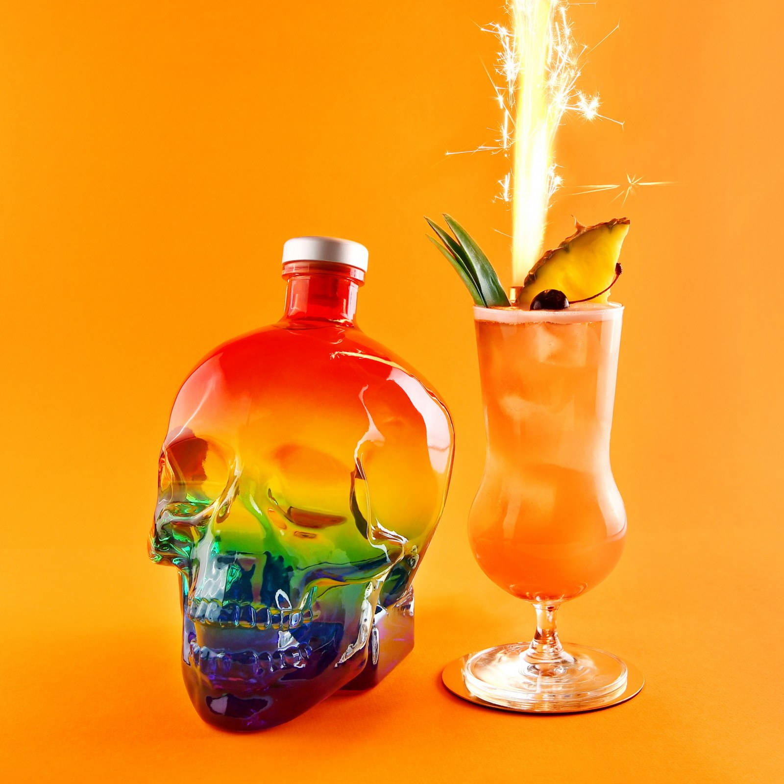 Drink 桌布 壁紙 — 彩虹骷髏瓶和熱帶雞尾酒，搭配煙火裝飾，襯托鮮豔橙色背景。