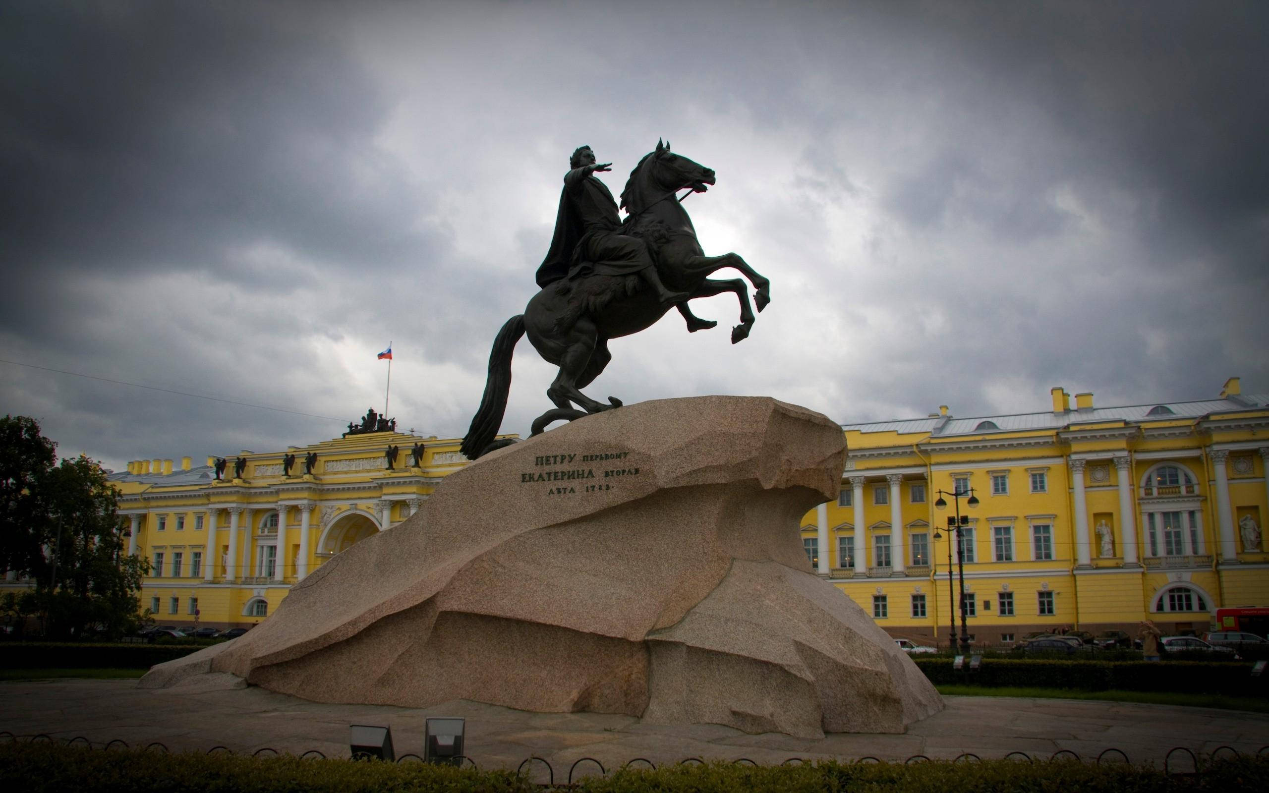 Saint Petersburg 桌布 壁紙 — 彼得大帝的戲劇性騎馬雕像在巨大石基座上揚起，背景是暴風雨的天空和一座宏偉的黃色宮殿。