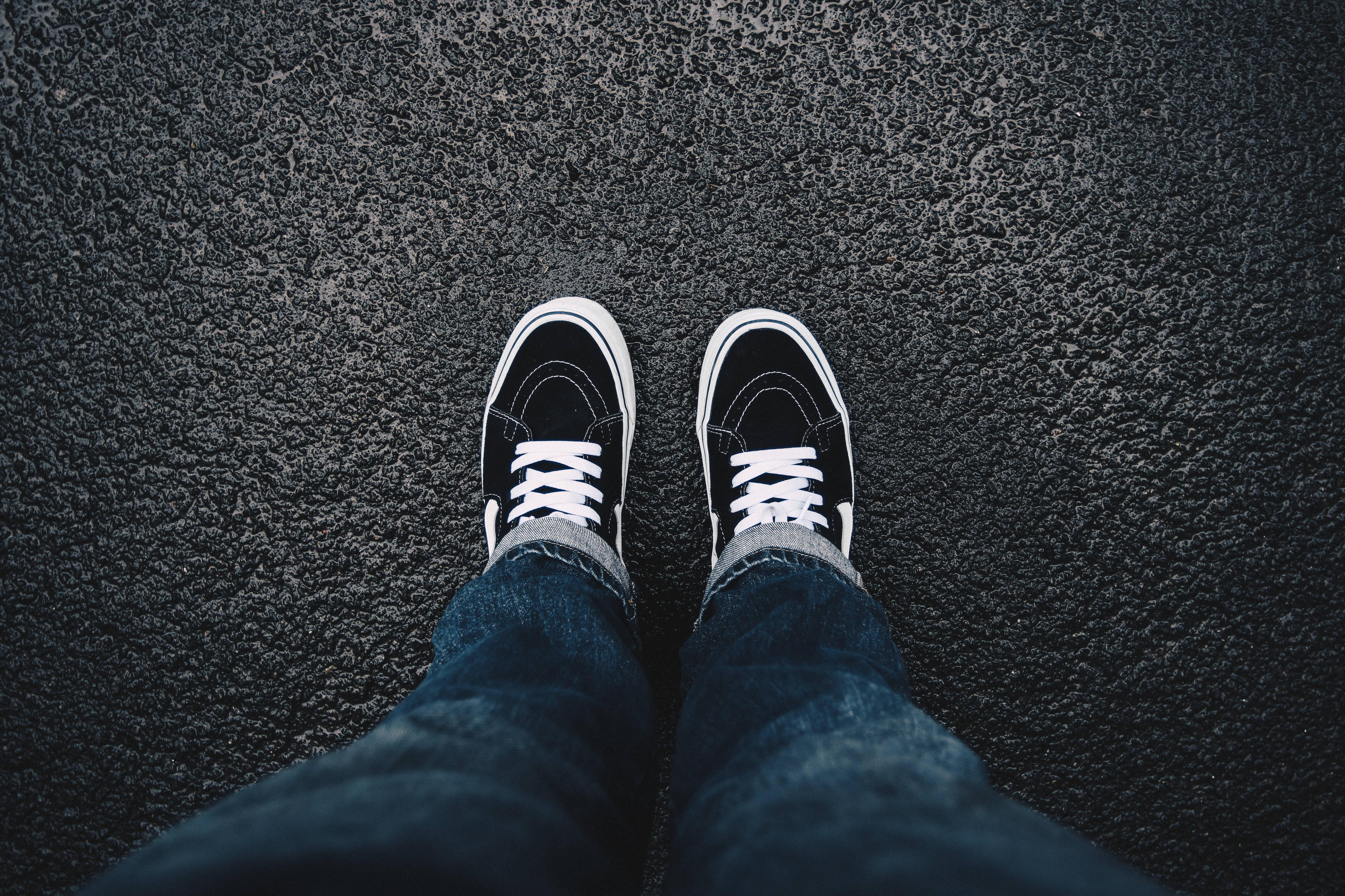 Vans 桌布 壁紙 — 從上往下看的雙腳，穿著黑色運動鞋配白色鞋帶，站在有紋理的瀝青地上。