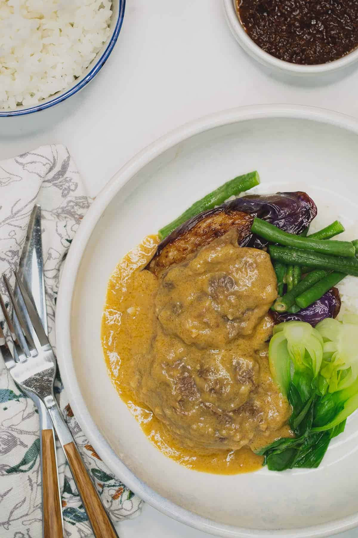 meat 桌布 壁紙 — 從上方俯瞰，一碗奶油牛肉燉菜搭配青豆和小白菜，放在白色碗中，旁邊有一碗白飯和一小碟深色醬汁。