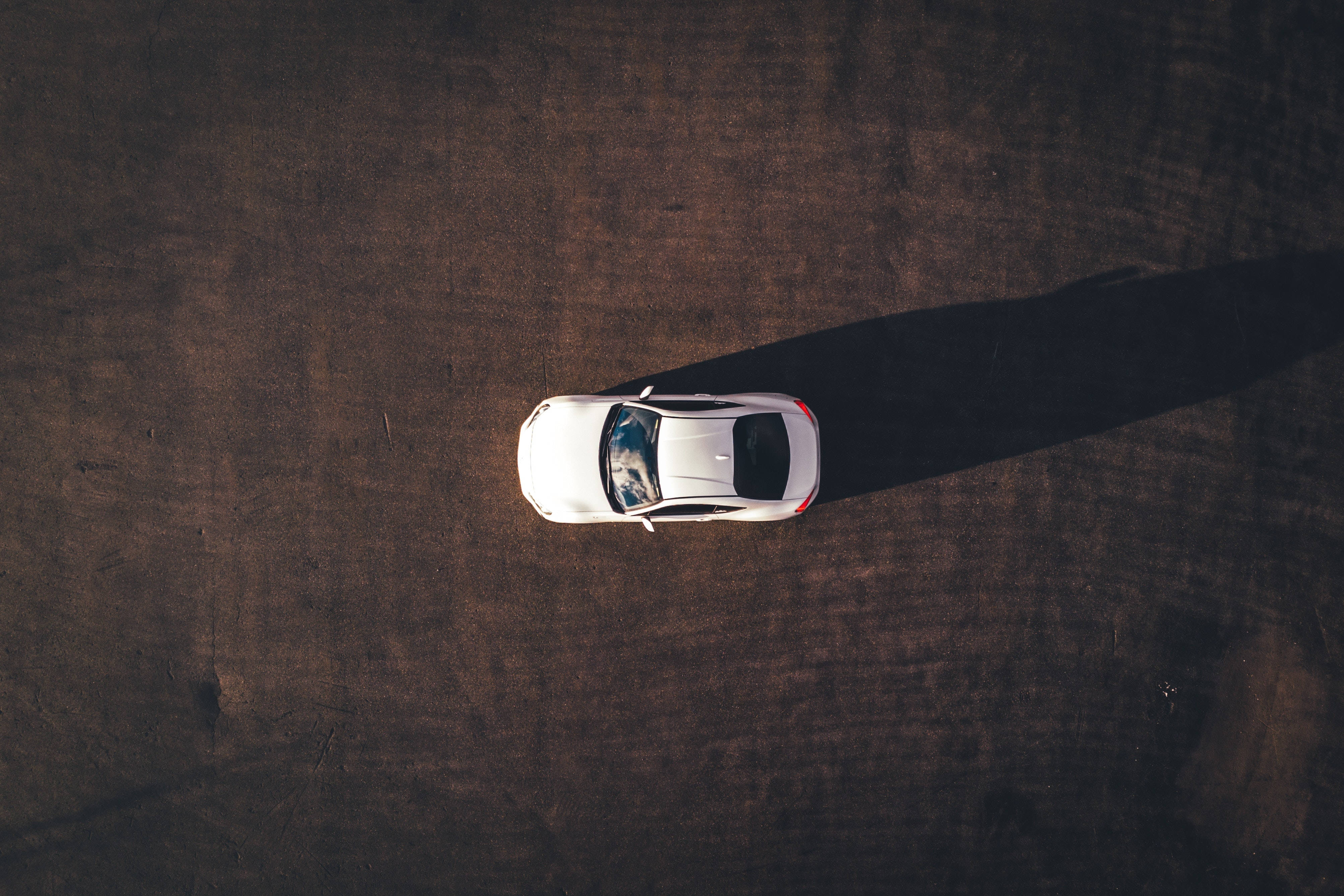Cool Car 桌布 壁紙 — 從上方俯瞰，一輛白色跑車在明亮的陽光下，在質感豐富的棕色泥地上投下長長的影子。