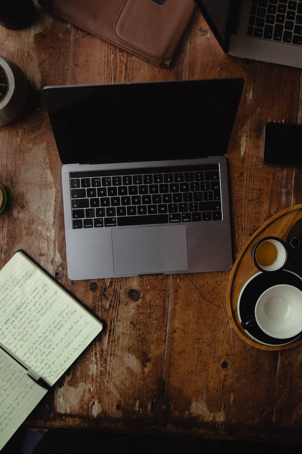 Best Laptop 桌布 壁紙 — 從上方俯瞰，一部銀色筆記型電腦放在質樸的木桌上，旁邊有筆記本、咖啡和電話。