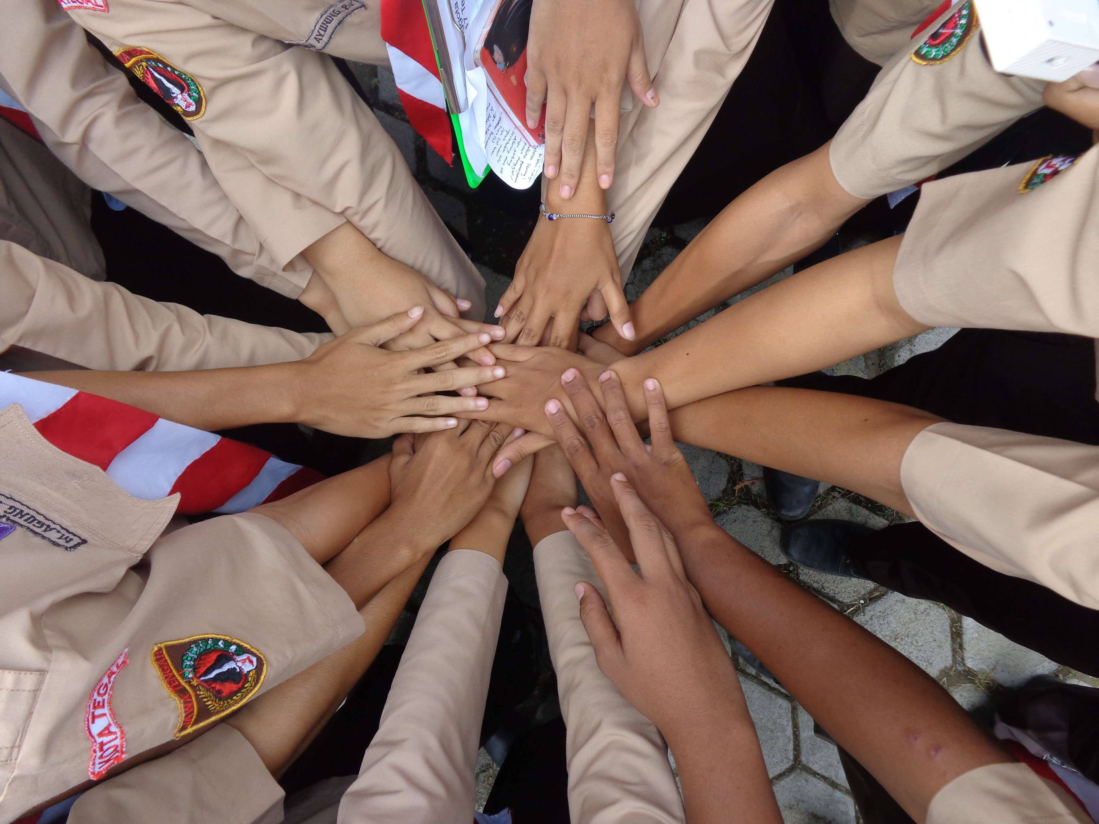 Teamwork 桌布 壁紙 — 從上方俯瞰，不同年輕人的手疊成一個圓圈，穿著帶有徽章的米色童軍制服。