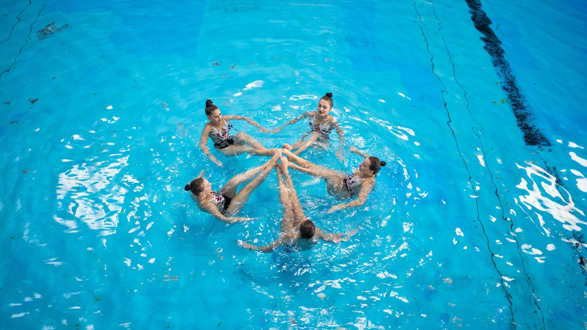 Swimming 桌布 壁紙 — 從上方俯瞰，五名韻律泳選手在充滿活力的藍色泳池水中手牽手形成一個圓圈。