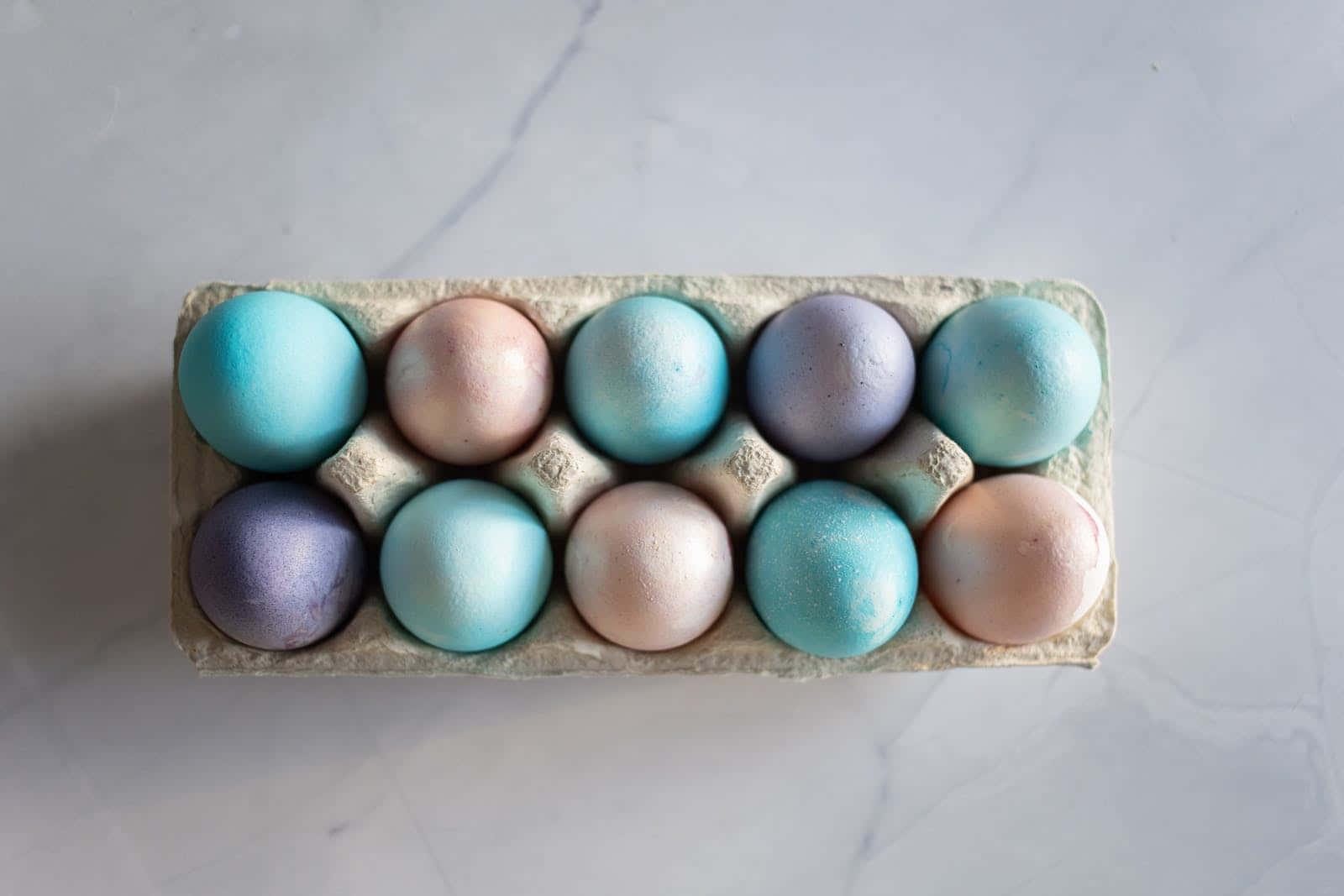 Eggs 桌布 壁紙 — 從上方俯瞰，大理石表面上一個紙板盒中放著粉彩色的雞蛋。