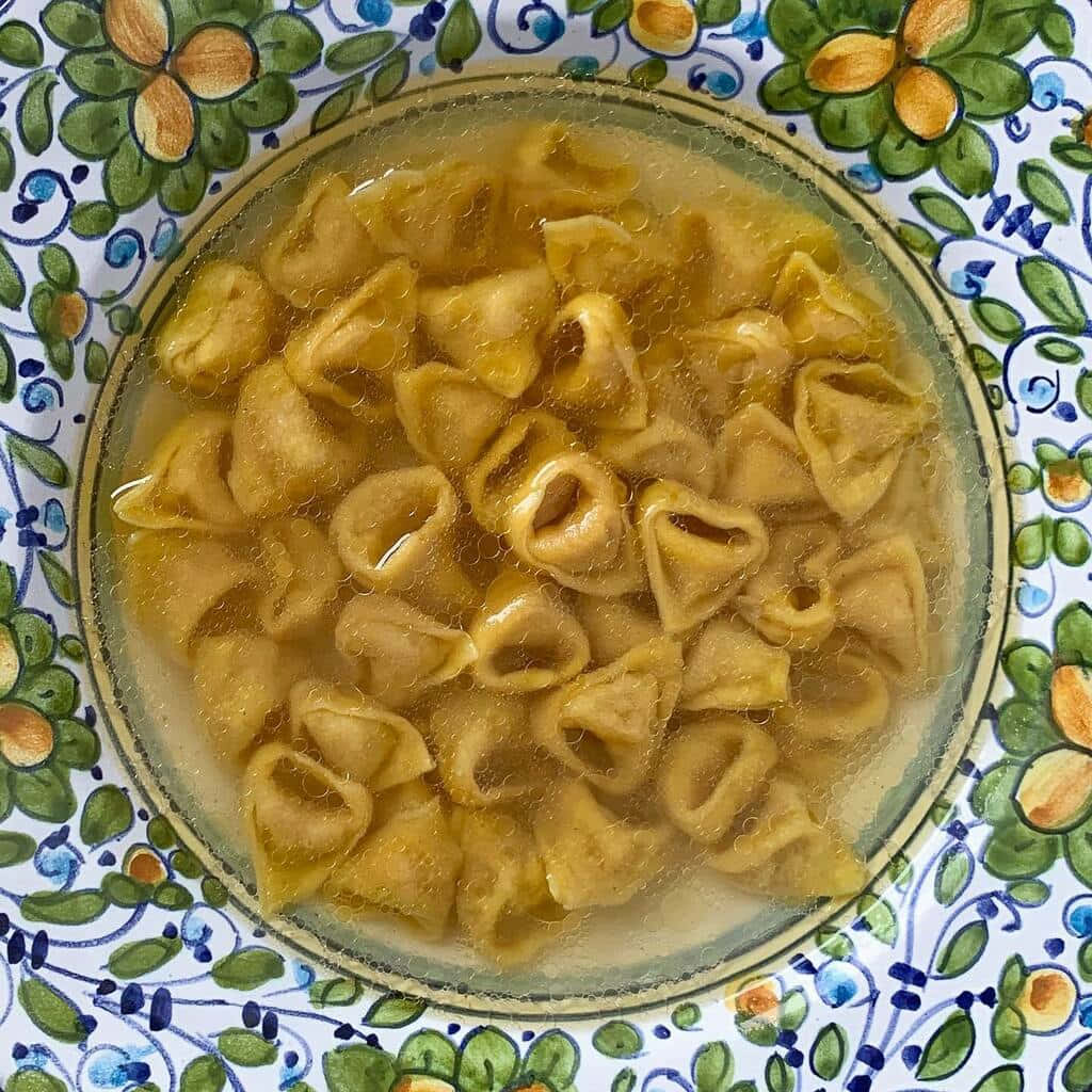 Pasta 桌布 壁紙 — 從上方俯瞰，玻璃碗中的高湯義大利餃放在彩色花卉盤上。