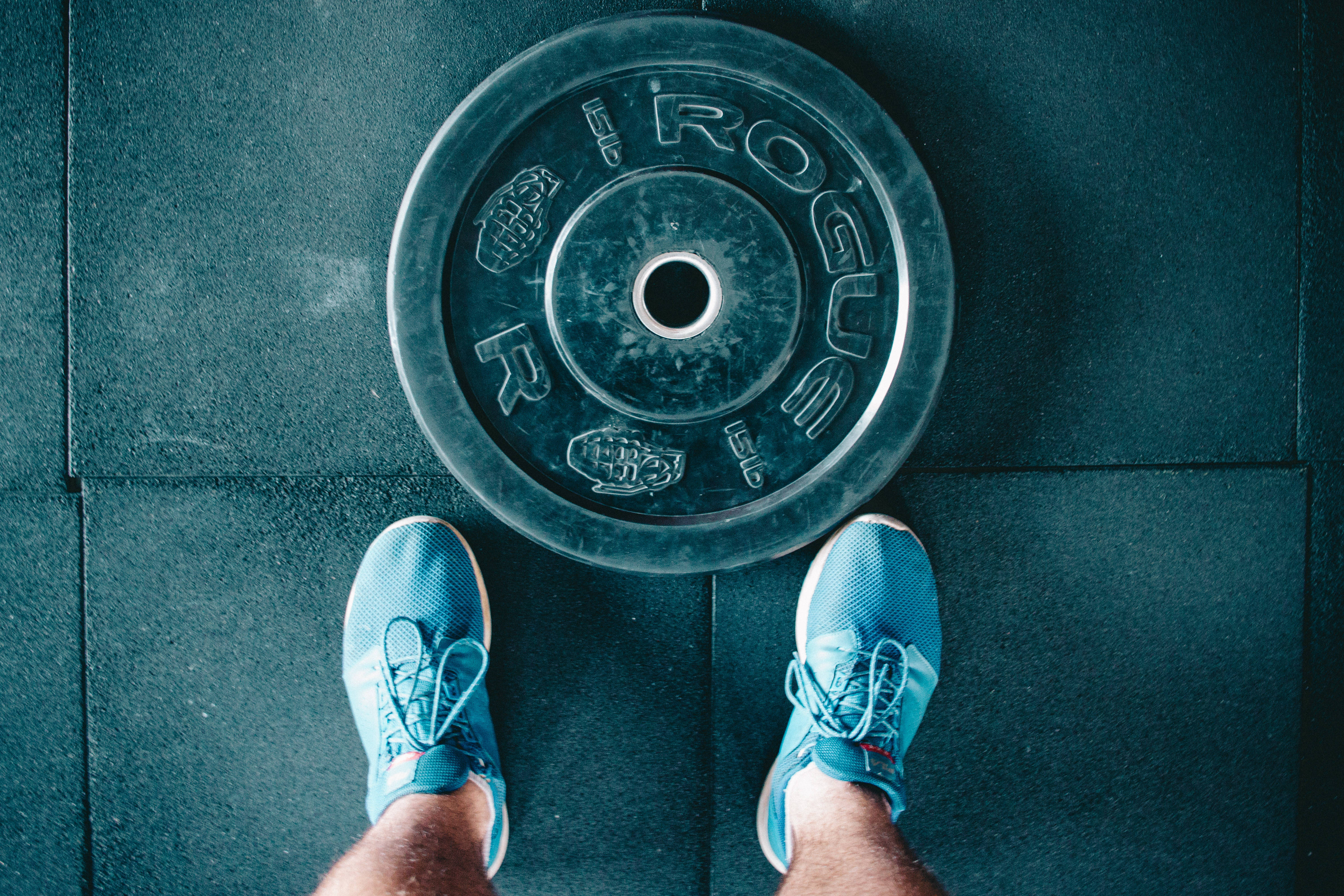 Fitness 桌布 壁紙 — 從上方俯瞰，藍色運動鞋站在深色健身房地板上的重型Rogue槓鈴片前。
