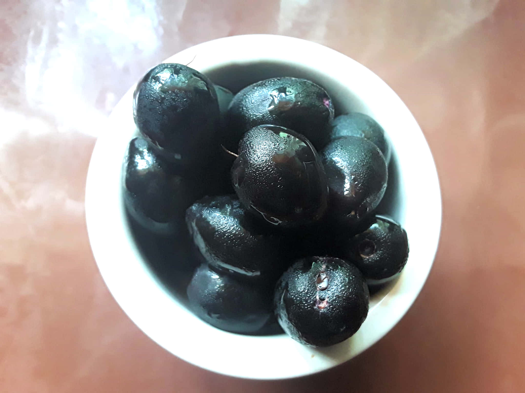 bowl 桌布 壁紙 — 從上方俯瞰，閃亮的黑橄欖在白色陶瓷碗中閃爍，置於粉紅色表面上。