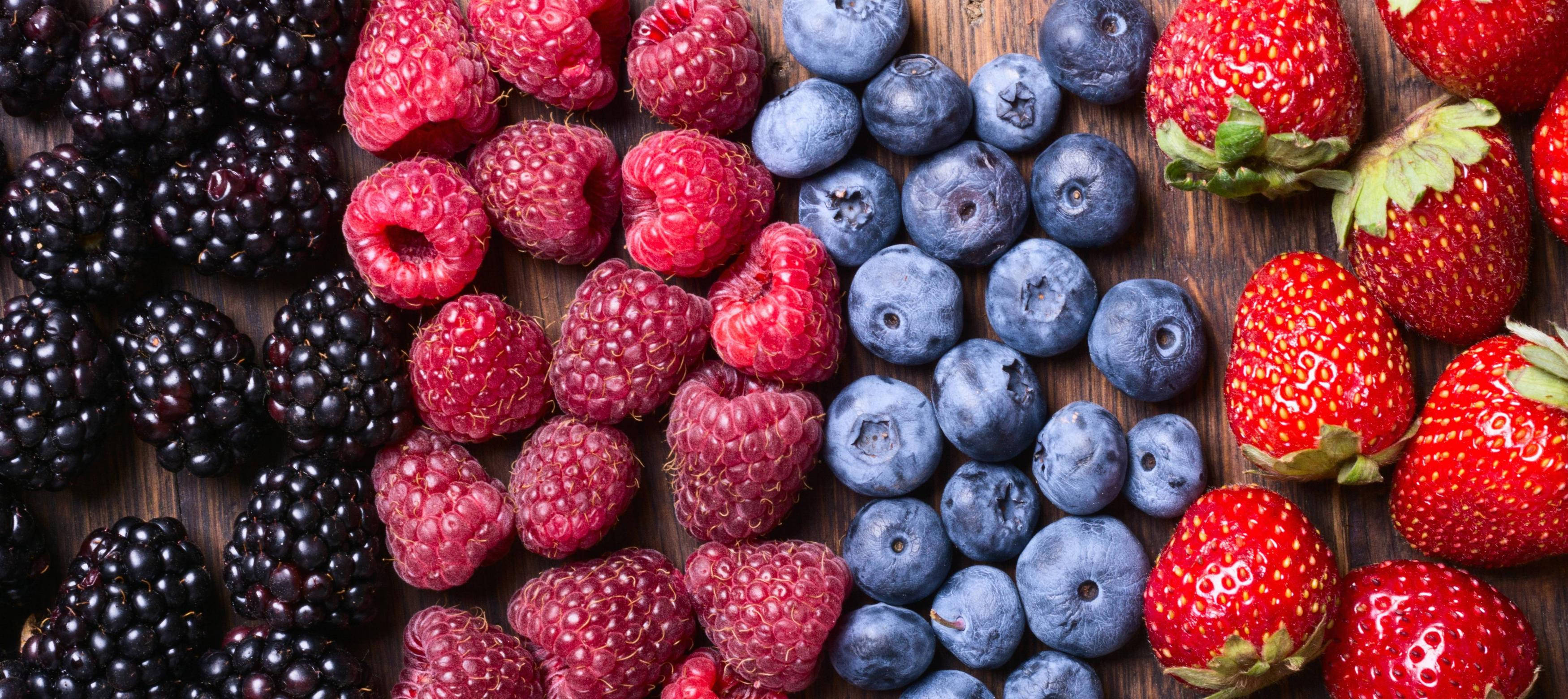 Berry 桌布 壁紙 — 從上方俯瞰，黑莓、覆盆子、藍莓和草莓整齊排列在質樸的木質表面上，色彩鮮豔。