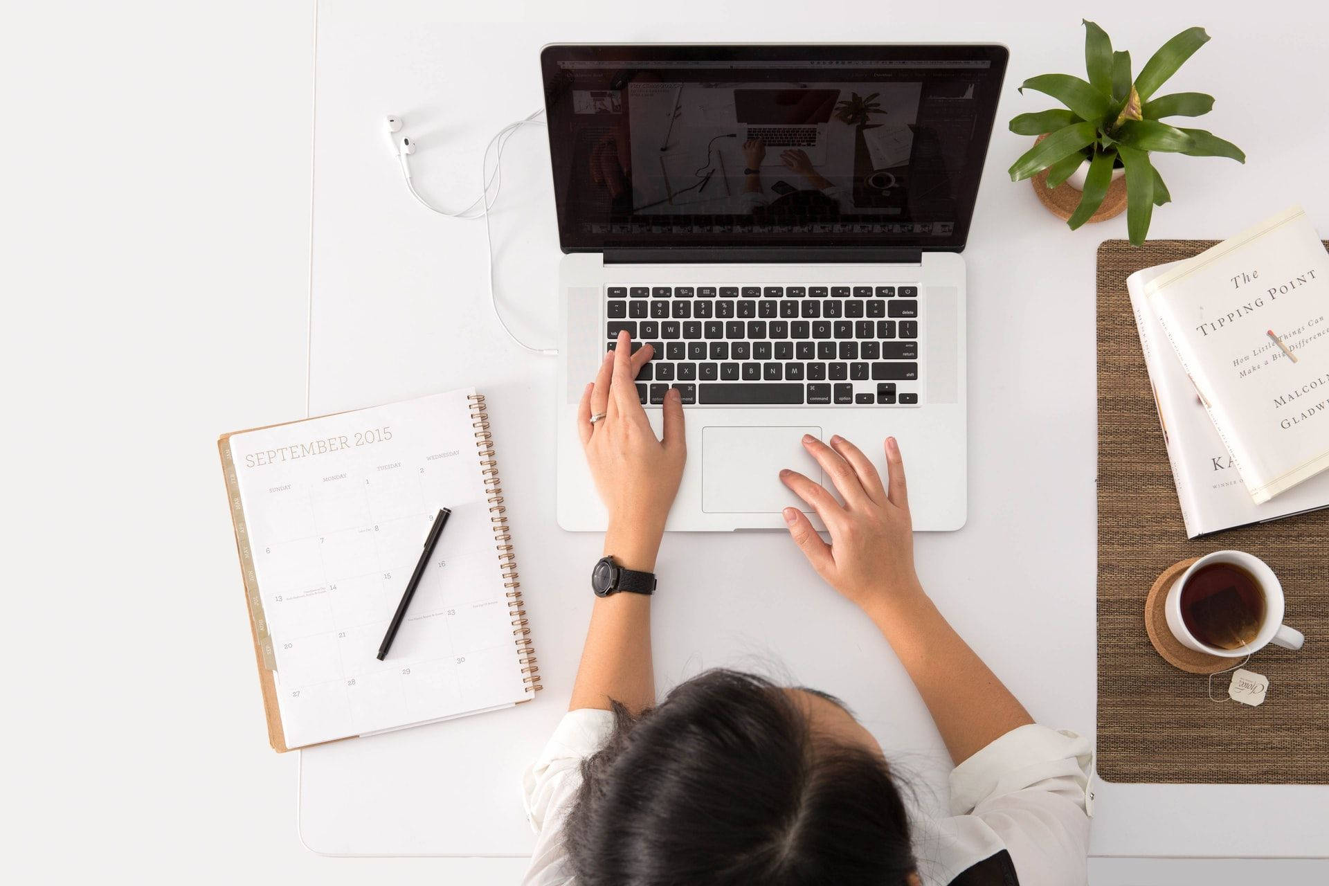 筆電 桌布 壁紙 — 從上方俯瞰一個人在簡約白色桌子上使用筆記型電腦打字，桌上放有日曆、咖啡和植物。