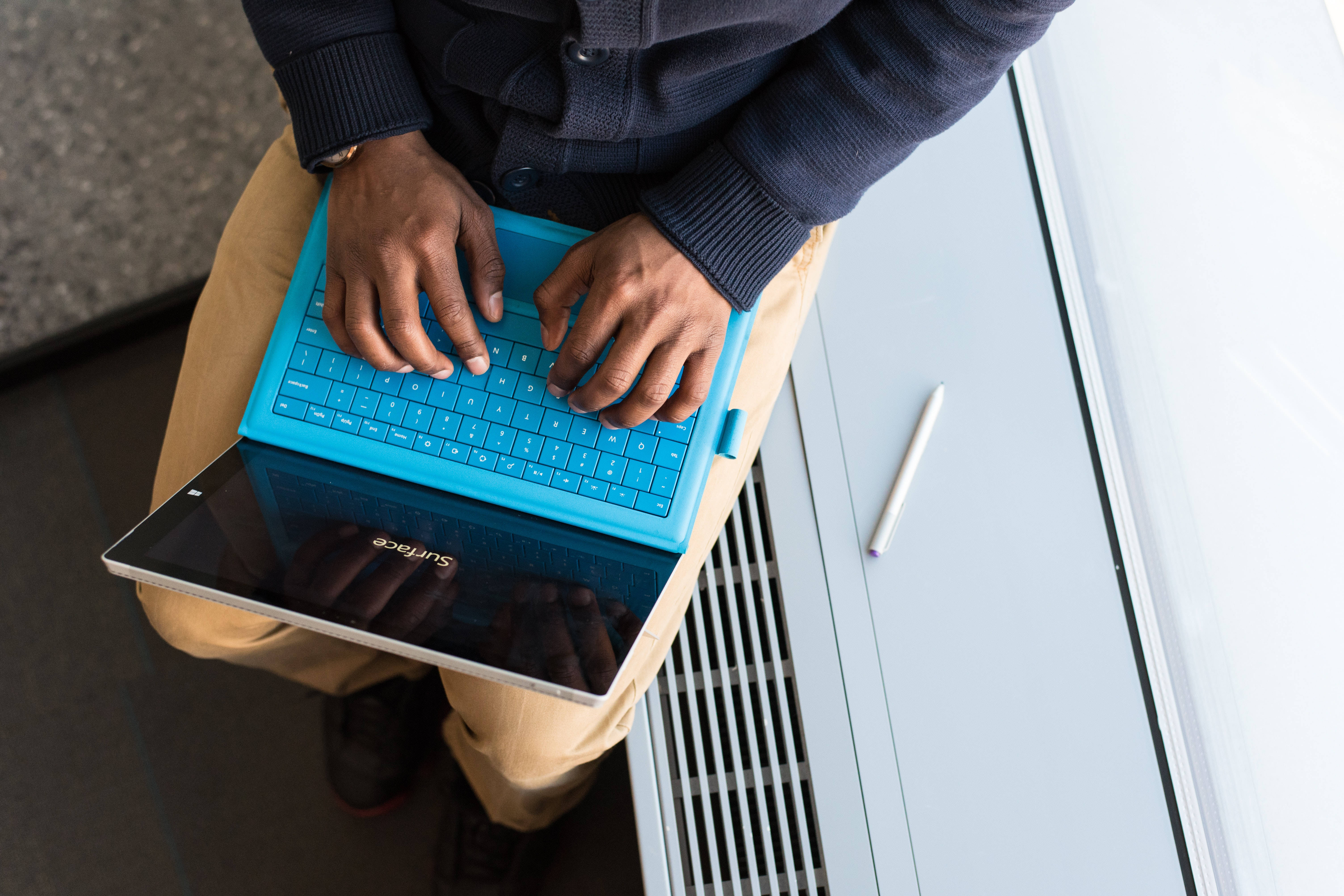 Cute Laptop 桌布 壁紙 — 從上方俯瞰一個人坐在現代白色長椅上，在亮藍色筆記型電腦上打字的景象。