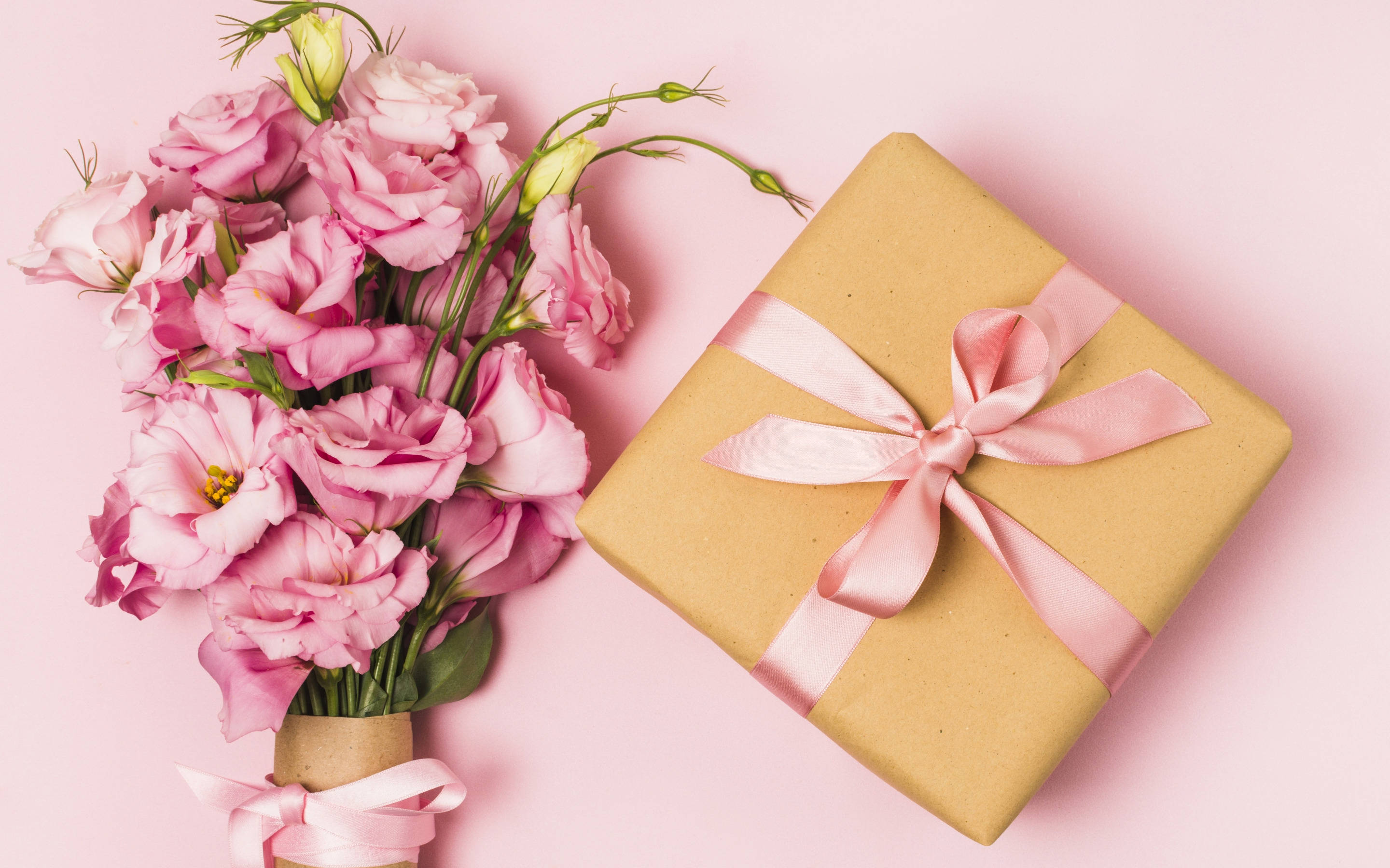 Happy Birthday Flower 桌布 壁紙 — 從上方俯瞰一個包裝好的禮物盒和粉紅色花朵，背景是柔和的粉紅色。