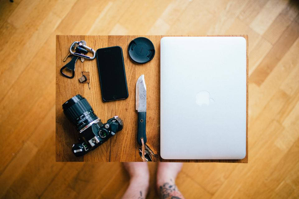 photography iPhone 桌布 壁紙 — 從上方俯瞰一個木板上放著相機、手機、筆記型電腦、刀和鑰匙在硬木地板上。