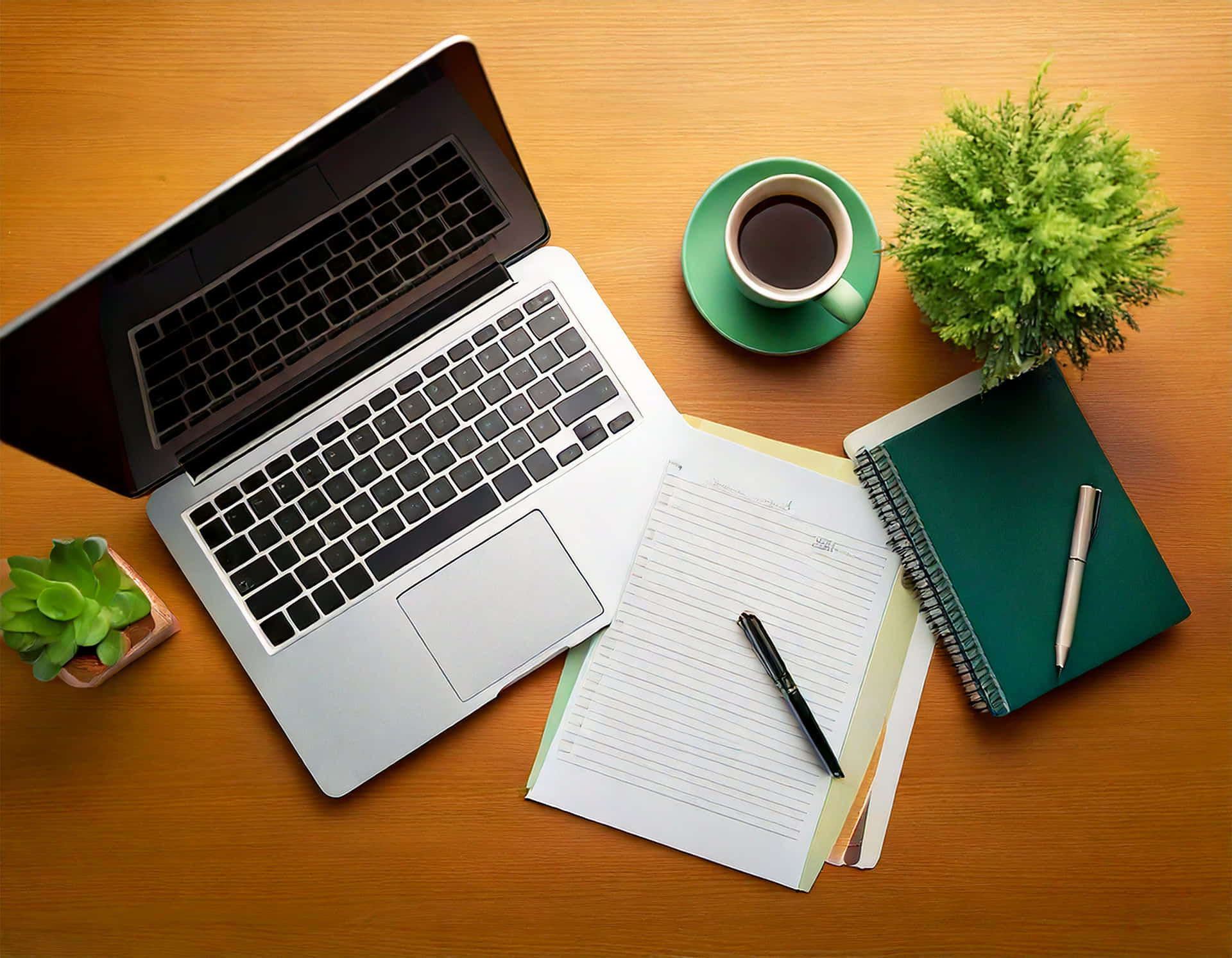 Elegant Office Workspace Scene 壁紙 — 從上方俯瞰一個木製書桌，上面有一台銀色筆記型電腦打開，旁邊有一個綠色咖啡杯、一本筆記本和兩棵小盆栽。