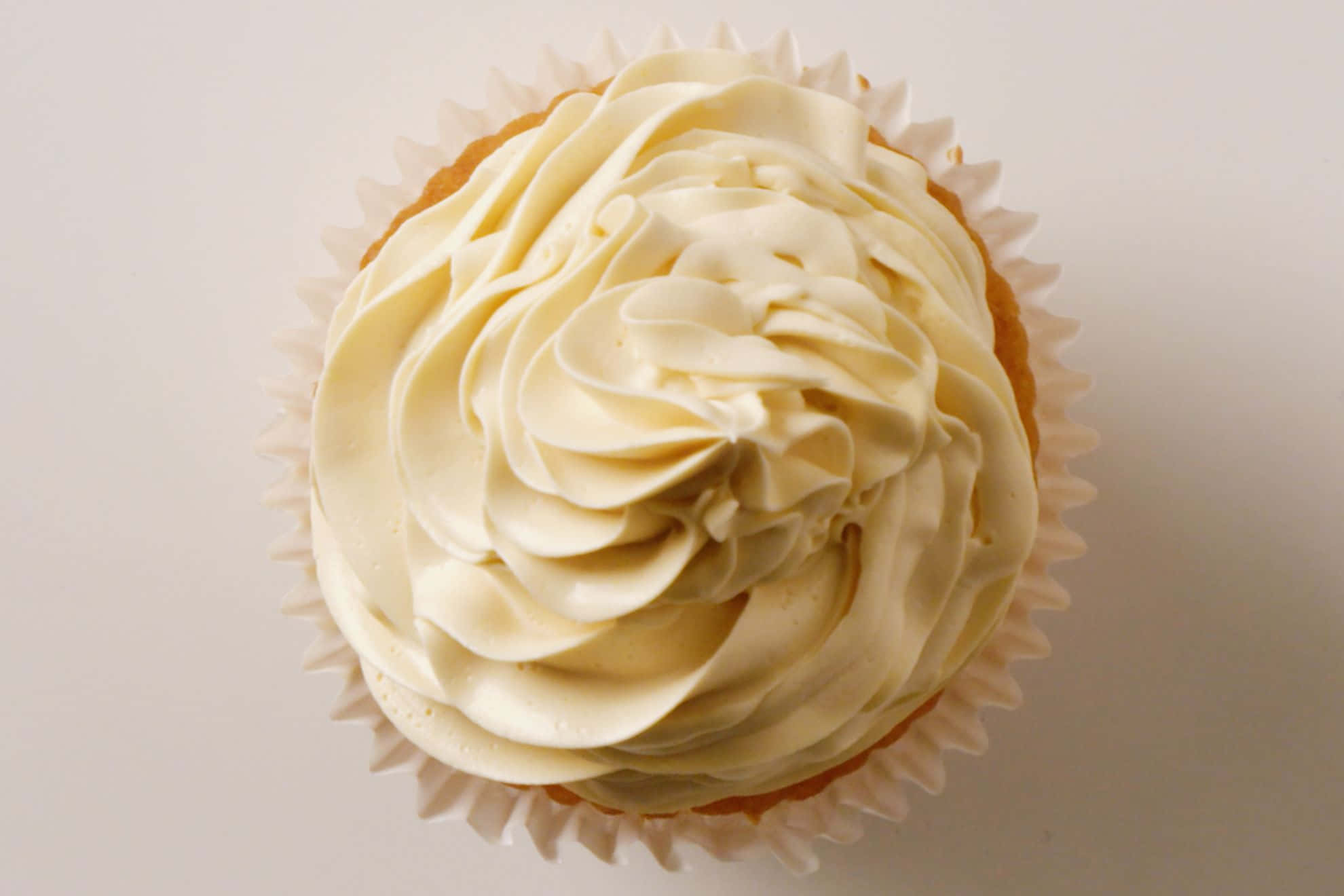 Buttercream 桌布 壁紙 — 從上方俯瞰一個杯子蛋糕，上面有奶油香草糖霜，在柔和的純色背景上形成優雅的尖峰。