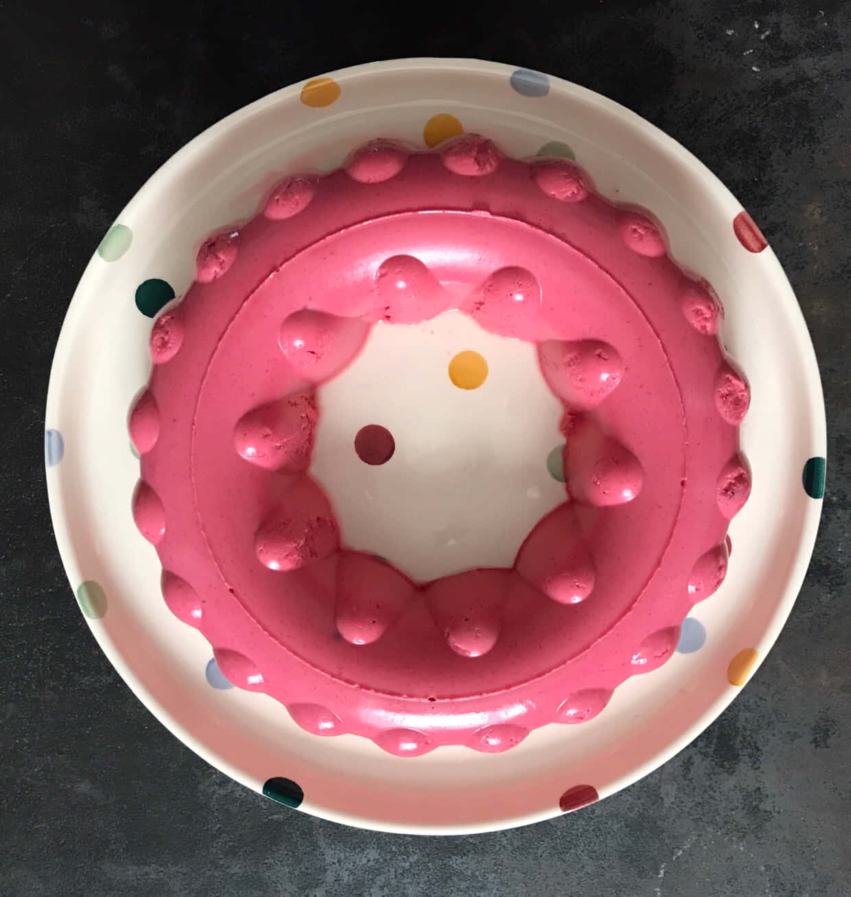 Blancmange 桌布 壁紙 — 從上方俯瞰一個深色檯面上的圓點碗中的粉紅色果凍甜品。