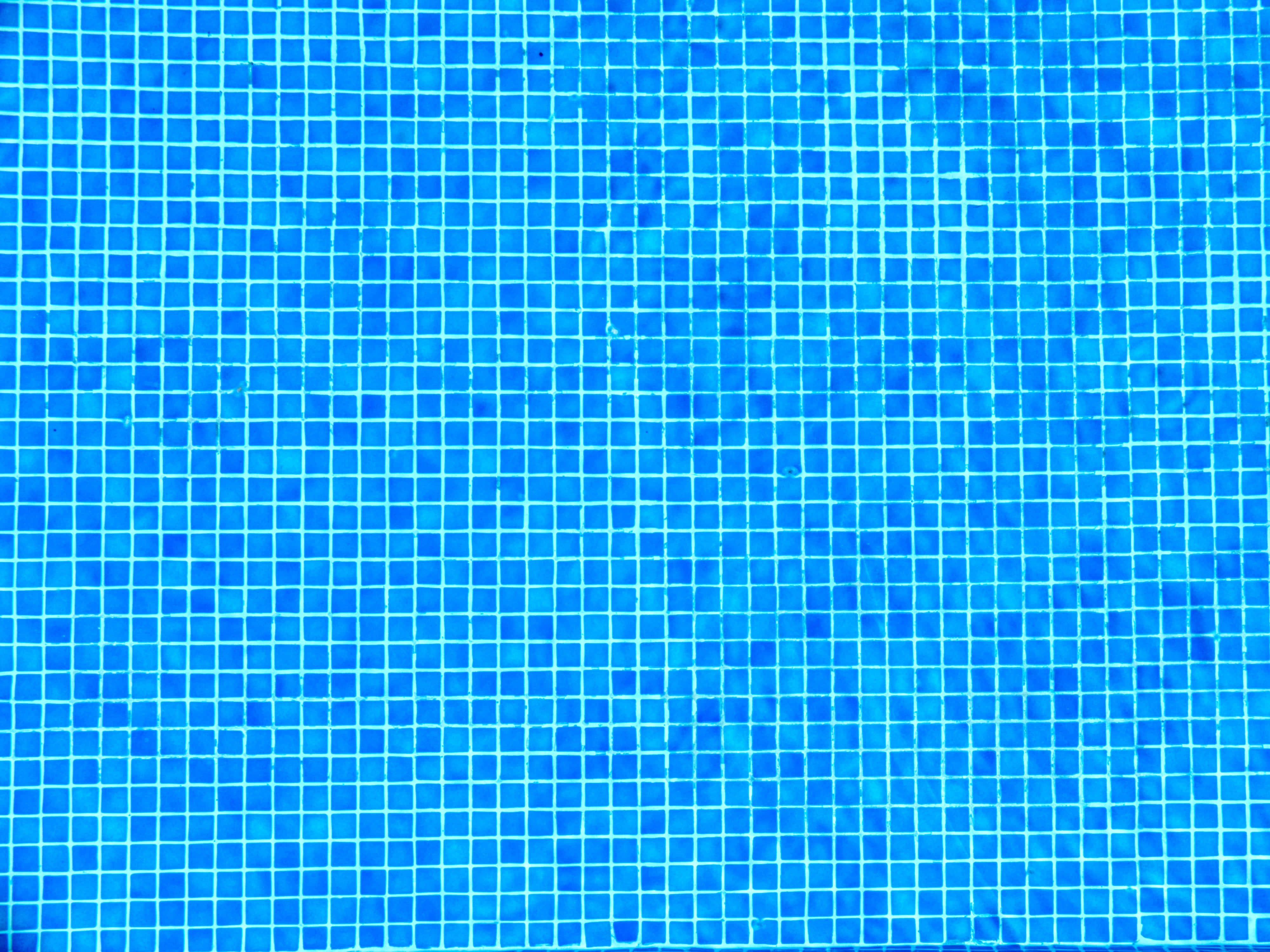 Blue Pattern 桌布 壁紙 — 從上方俯瞰一個游泳池，池底鋪滿細小的藍色方形瓷磚，在明亮光線下形成網格圖案。