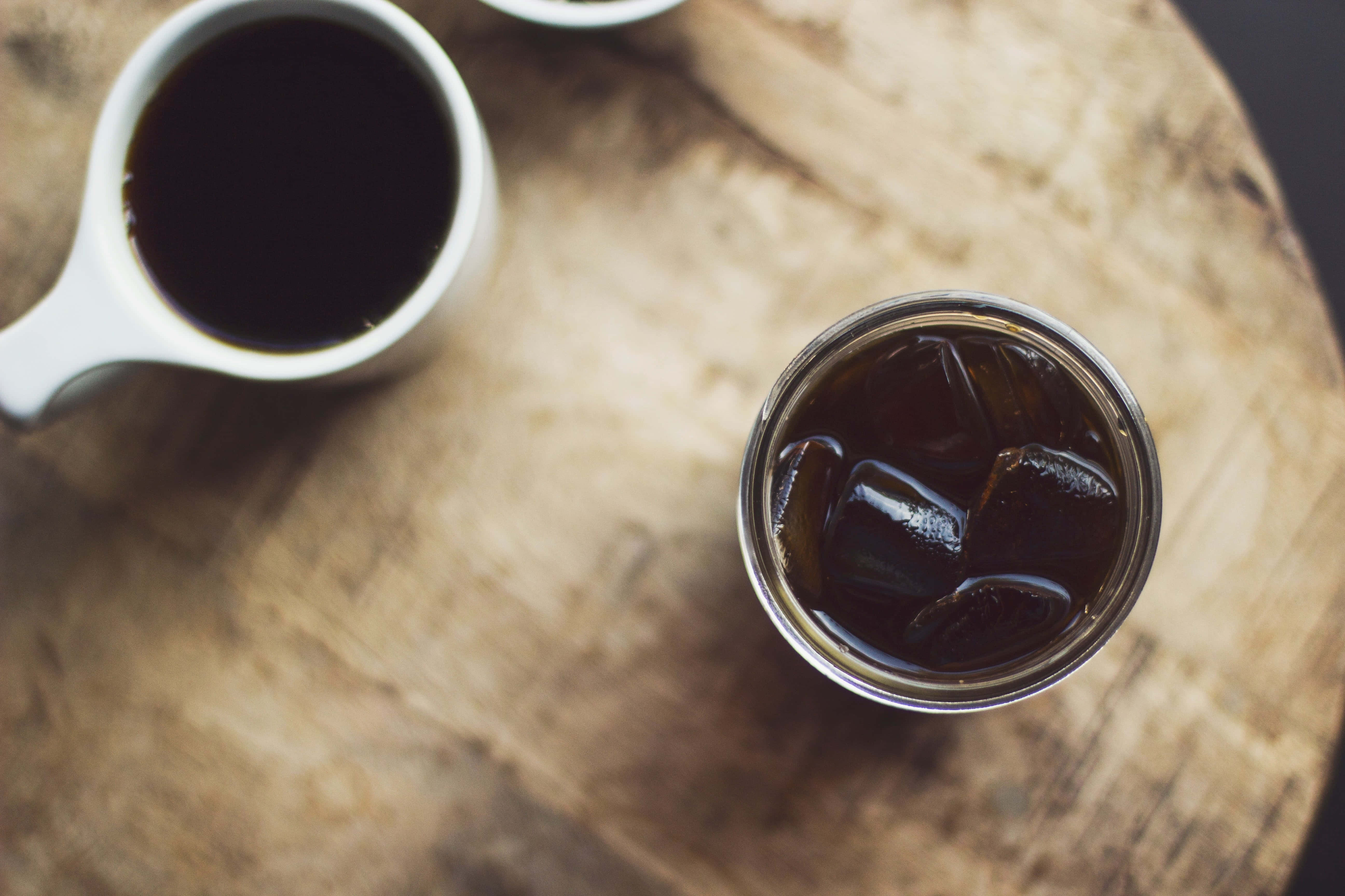 Iced Coffee 桌布 壁紙 — 從上方俯瞰一個白色馬克杯和一杯冰咖啡放在質樸的木桌上，光線柔和自然。