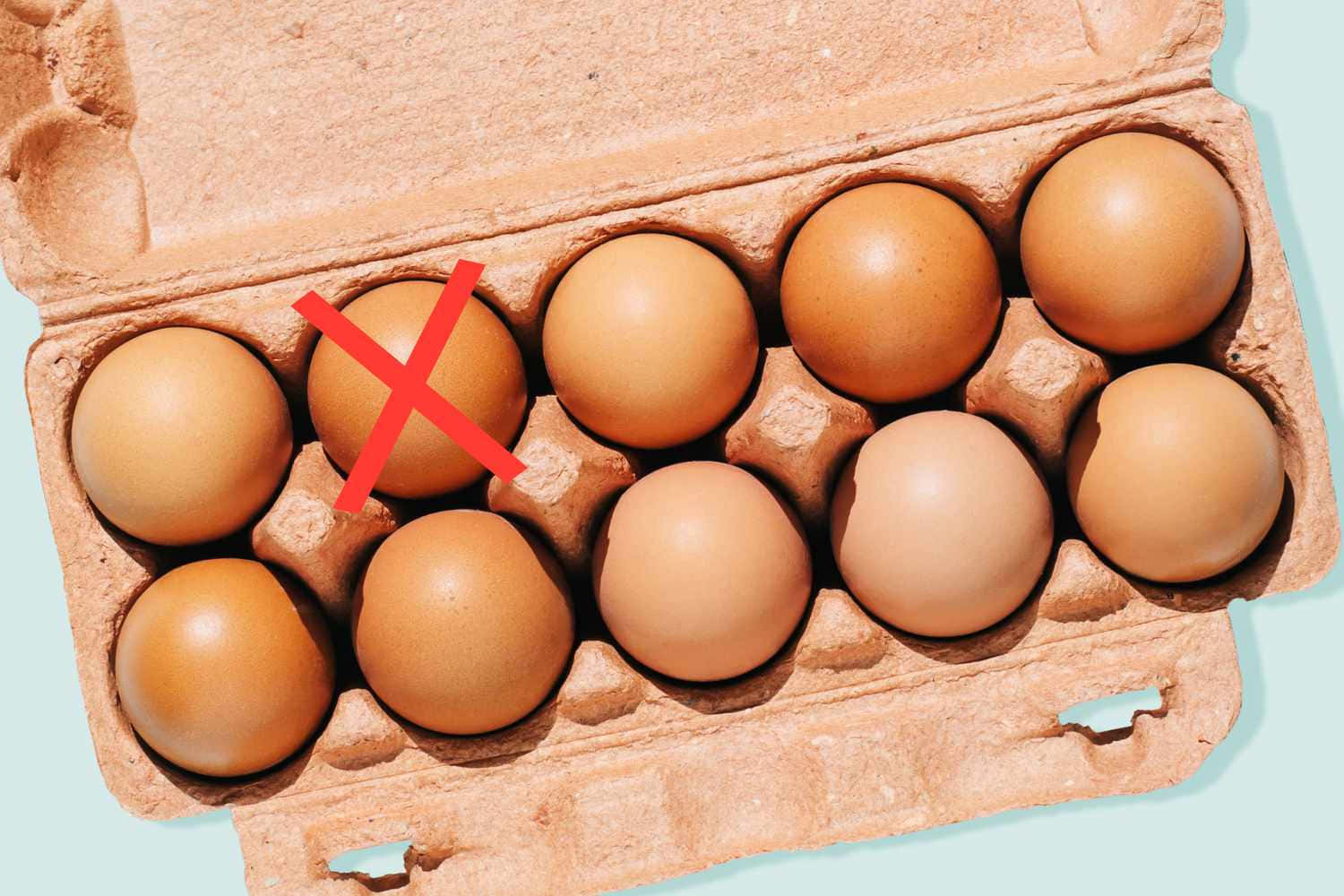 Egg 桌布 壁紙 — 從上方俯瞰一個紙板雞蛋盒，內有十顆棕色雞蛋，其中一顆標有紅色X記號，背景為淺藍色。