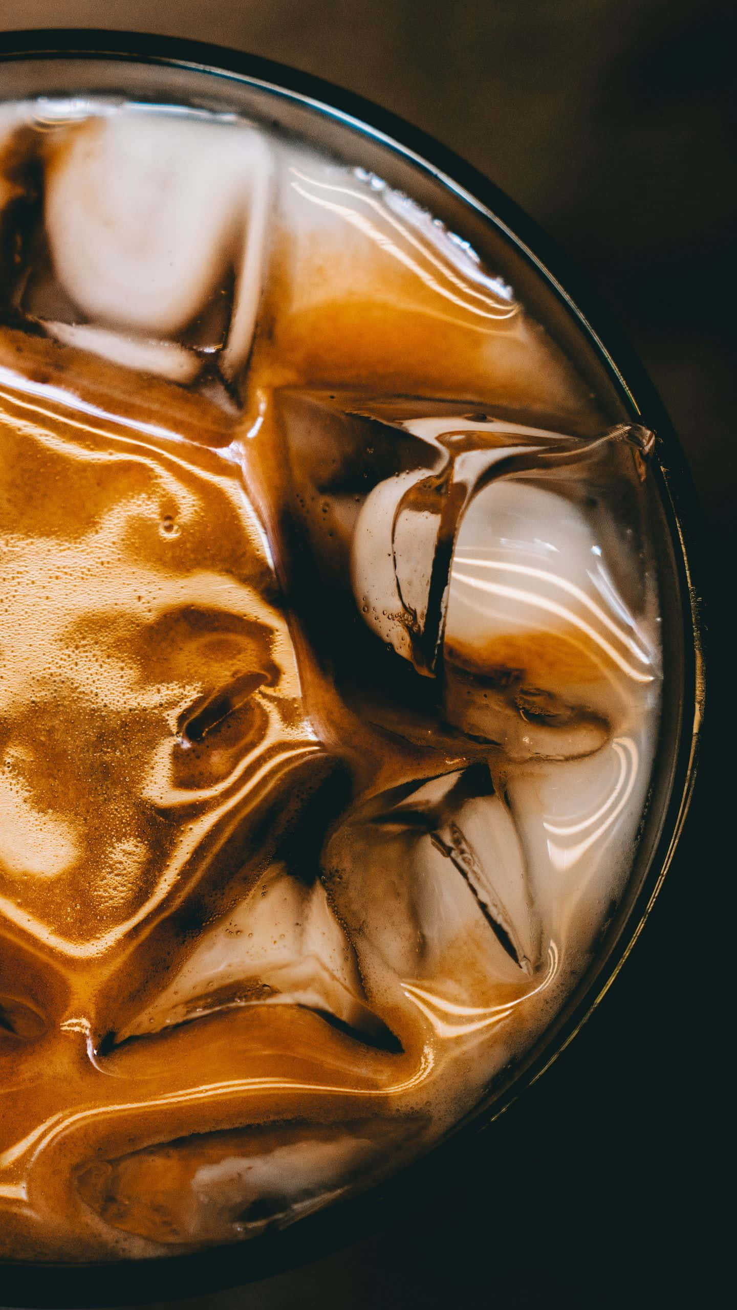 Iced Coffee 桌布 壁紙 — 從上方俯瞰一個裝滿冰咖啡和正在融化的冰塊，形成旋轉的棕色和白色圖案的玻璃杯。