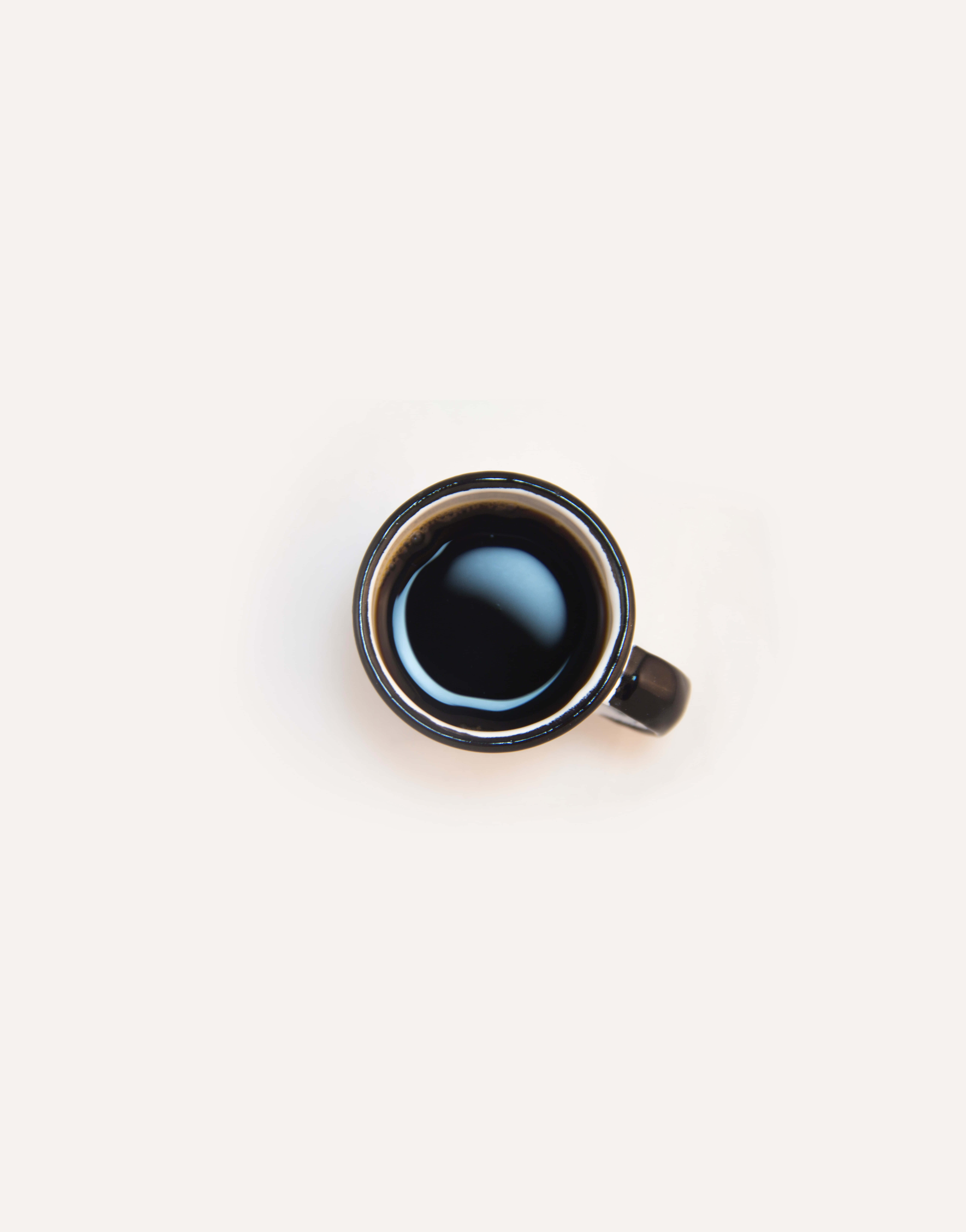 Minimalist Coffee 桌布 壁紙 — 從上方俯瞰一個裝滿黑咖啡的黑色陶瓷馬克杯，置於樸素的米白色表面上。