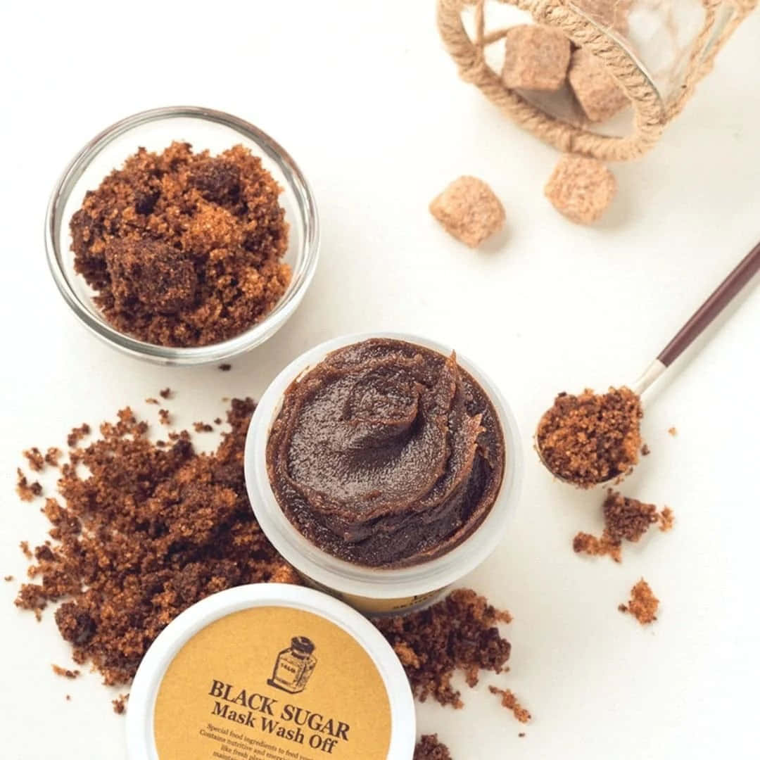 Black Sugar 桌布 壁紙 — 從上方俯瞰一個黑色糖面膜罐，帶有鬆散的顆粒和一匙糖在乾淨的白色表面上。