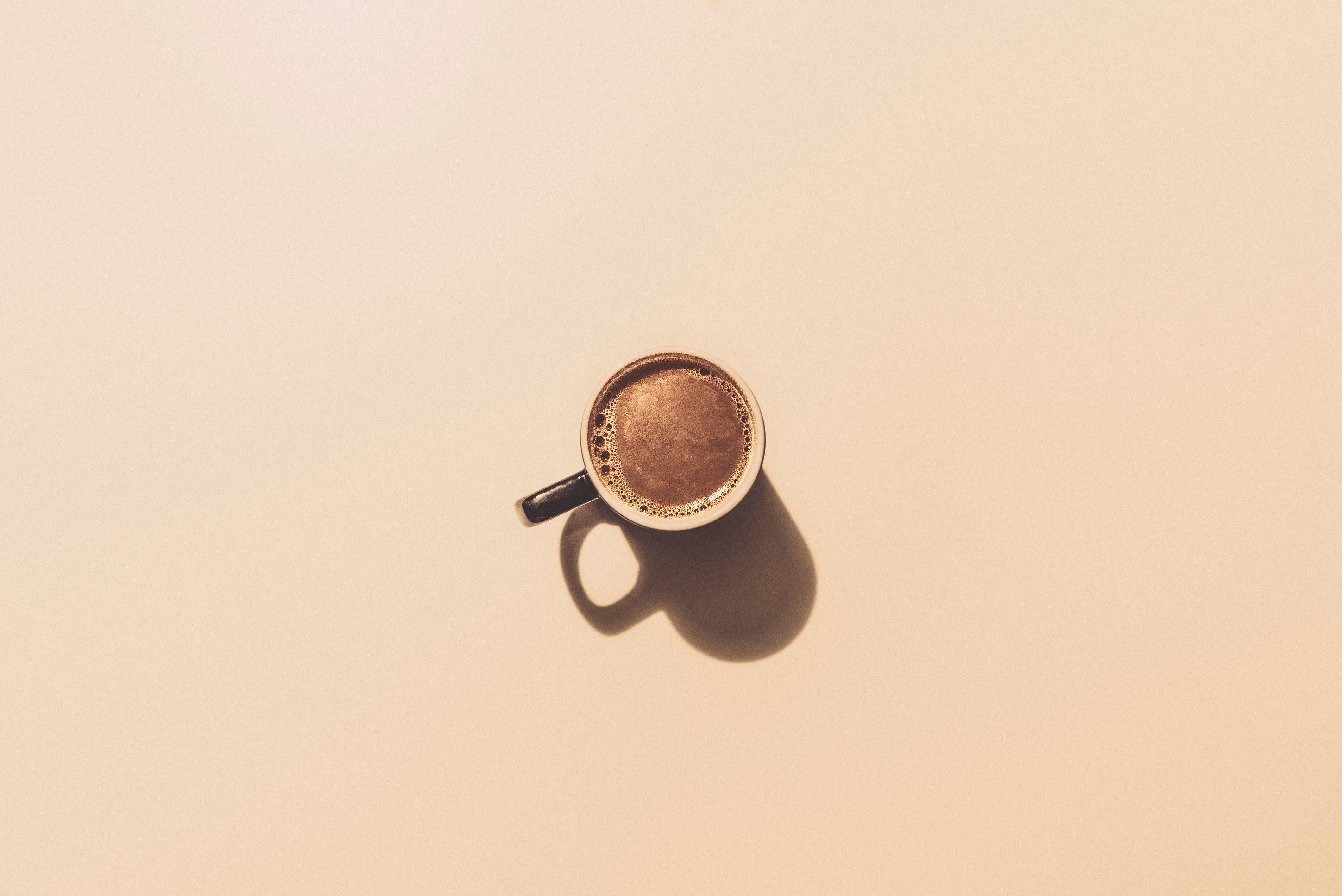 咖啡動圖 桌布 壁紙 — 從上方俯瞰一杯冒煙的咖啡杯，在溫暖的米色表面上投下柔和陰影。