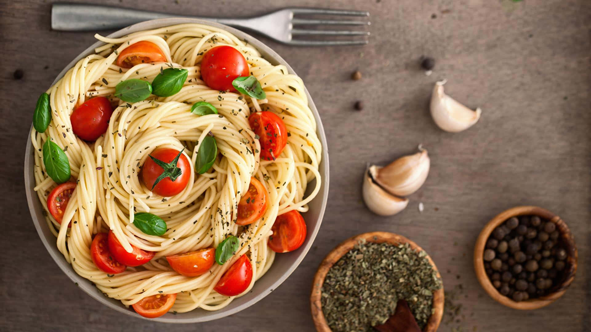 Pasta 桌布 壁紙 — 從上方俯瞰一碗義大利麵，上面鋪滿櫻桃番茄、羅勒和黑胡椒，置於質樸的木質表面上。