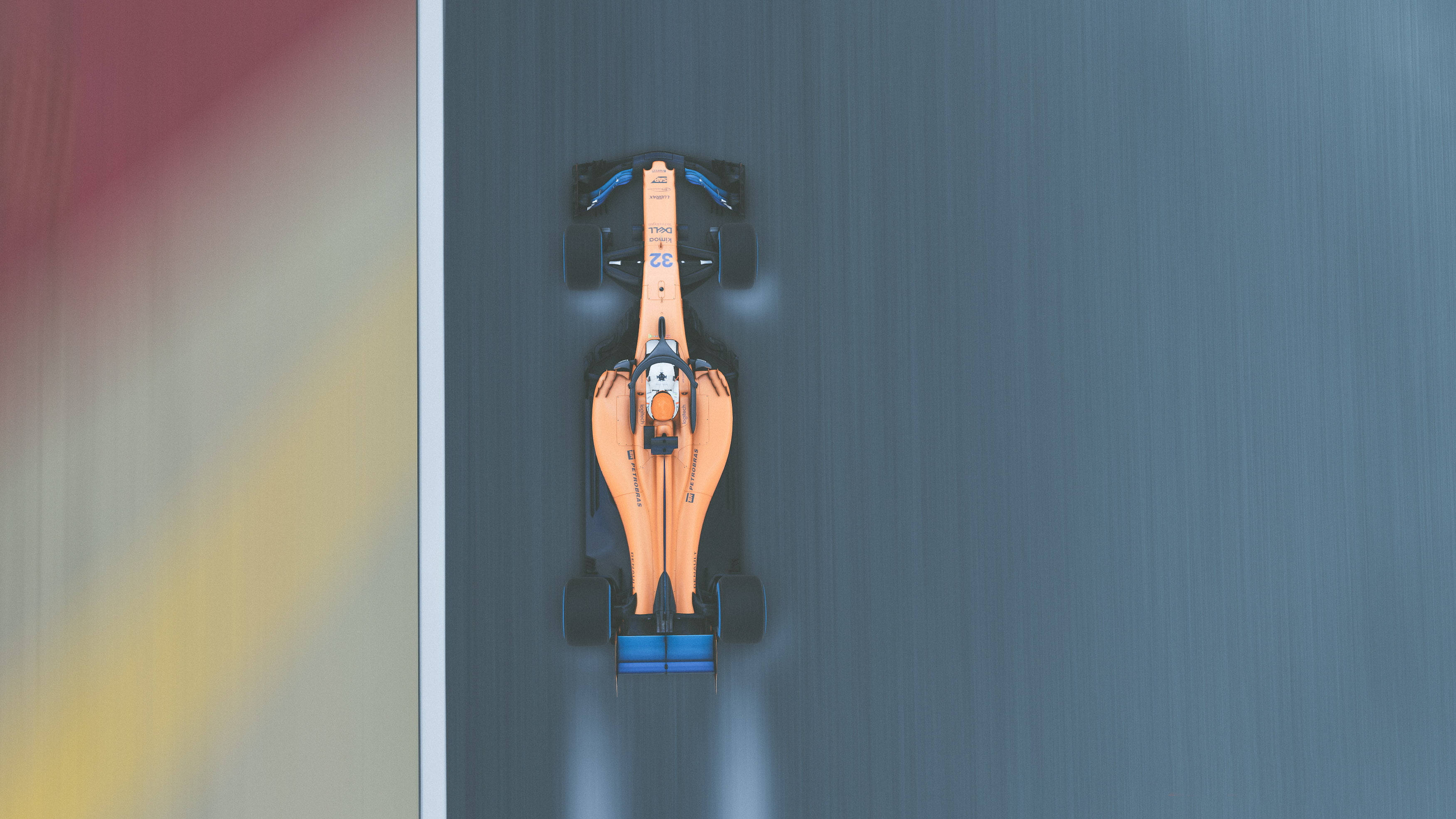 F1 桌布 壁紙 — 從上方俯瞰一輛橙色和藍色的F1賽車在賽道上疾馳，帶有動態模糊效果。
