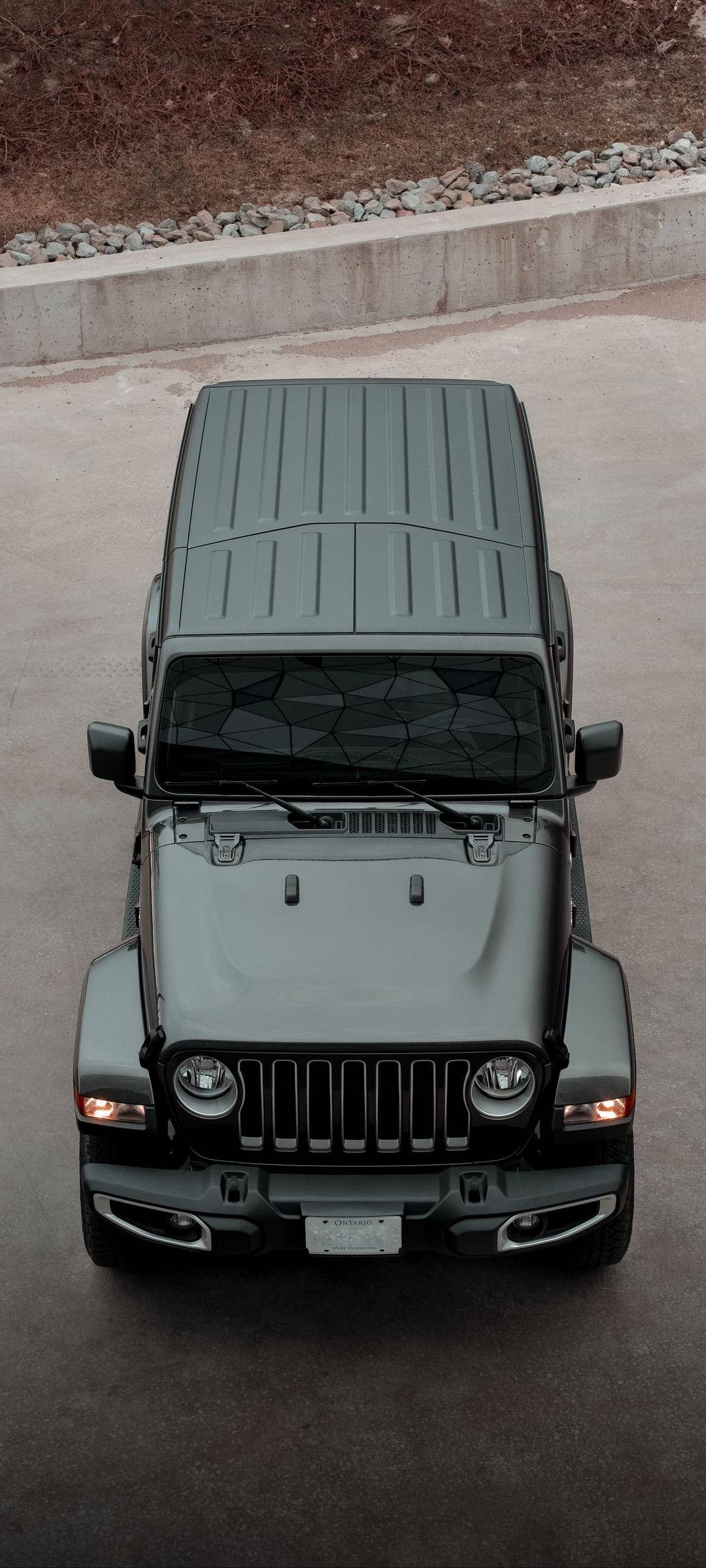Black Jeep 桌布 壁紙 — 從上方俯瞰一輛消光灰色Jeep Wrangler停在混凝土上，背景有碎石和混凝土牆。