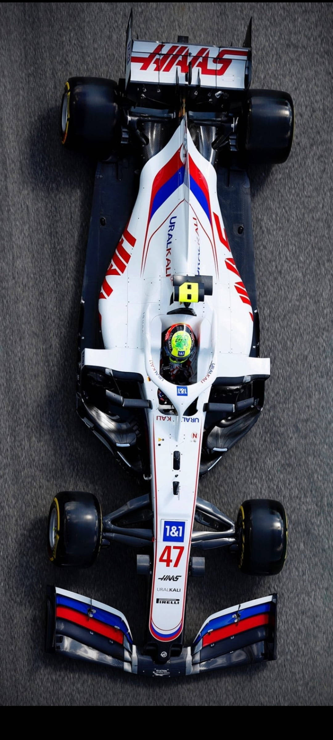 mick schumacher 桌布 壁紙 — 從上方俯瞰一輛白色、紅色和藍色的Haas F1賽車，車手號碼47，在灰色賽道表面上。