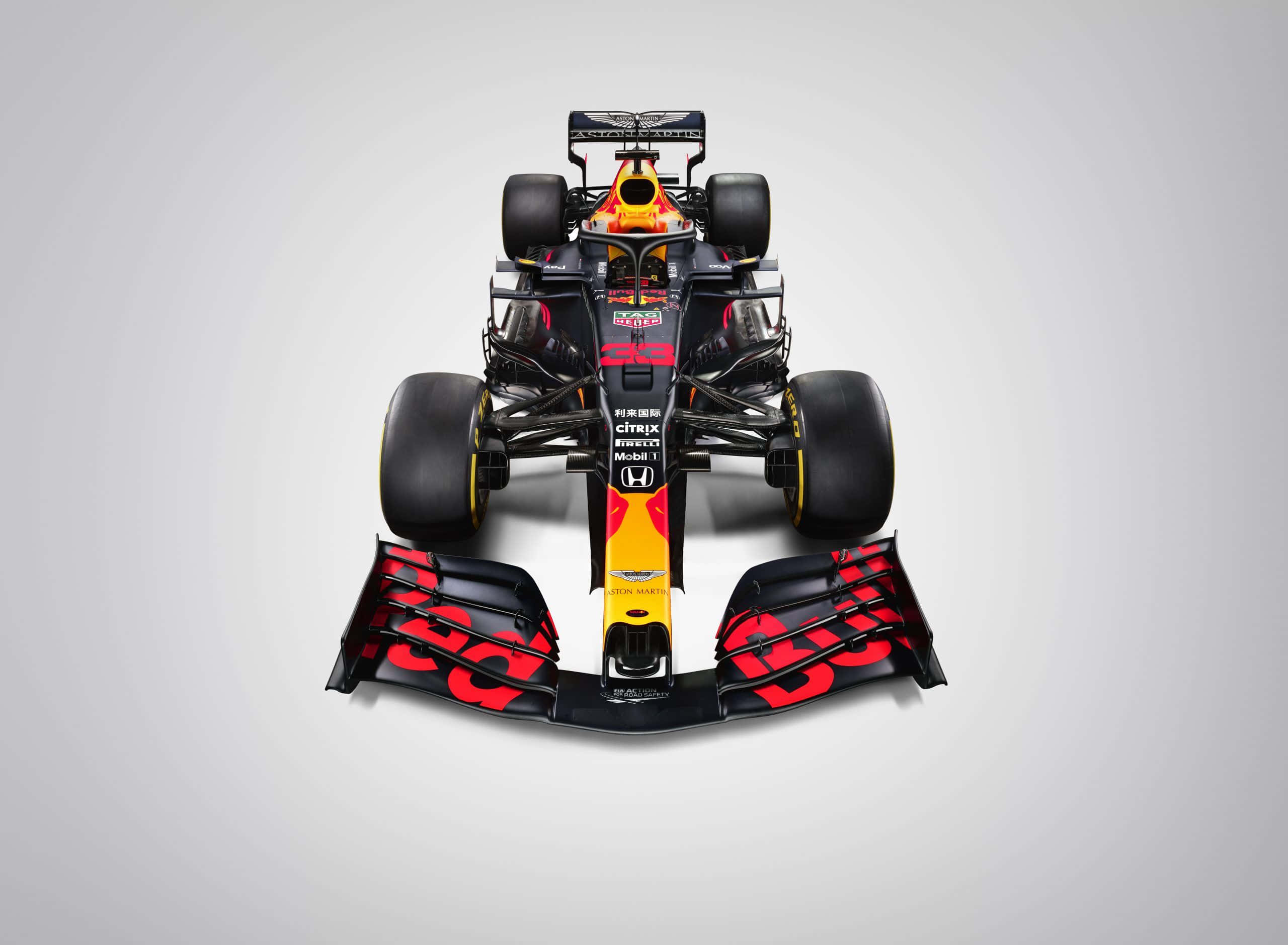 Max Verstappen 桌布 壁紙 — 從上方俯瞰一輛紅牛車隊一級方程式賽車，車身採用大膽的紅、黑、黃配色，背景為中性灰色。