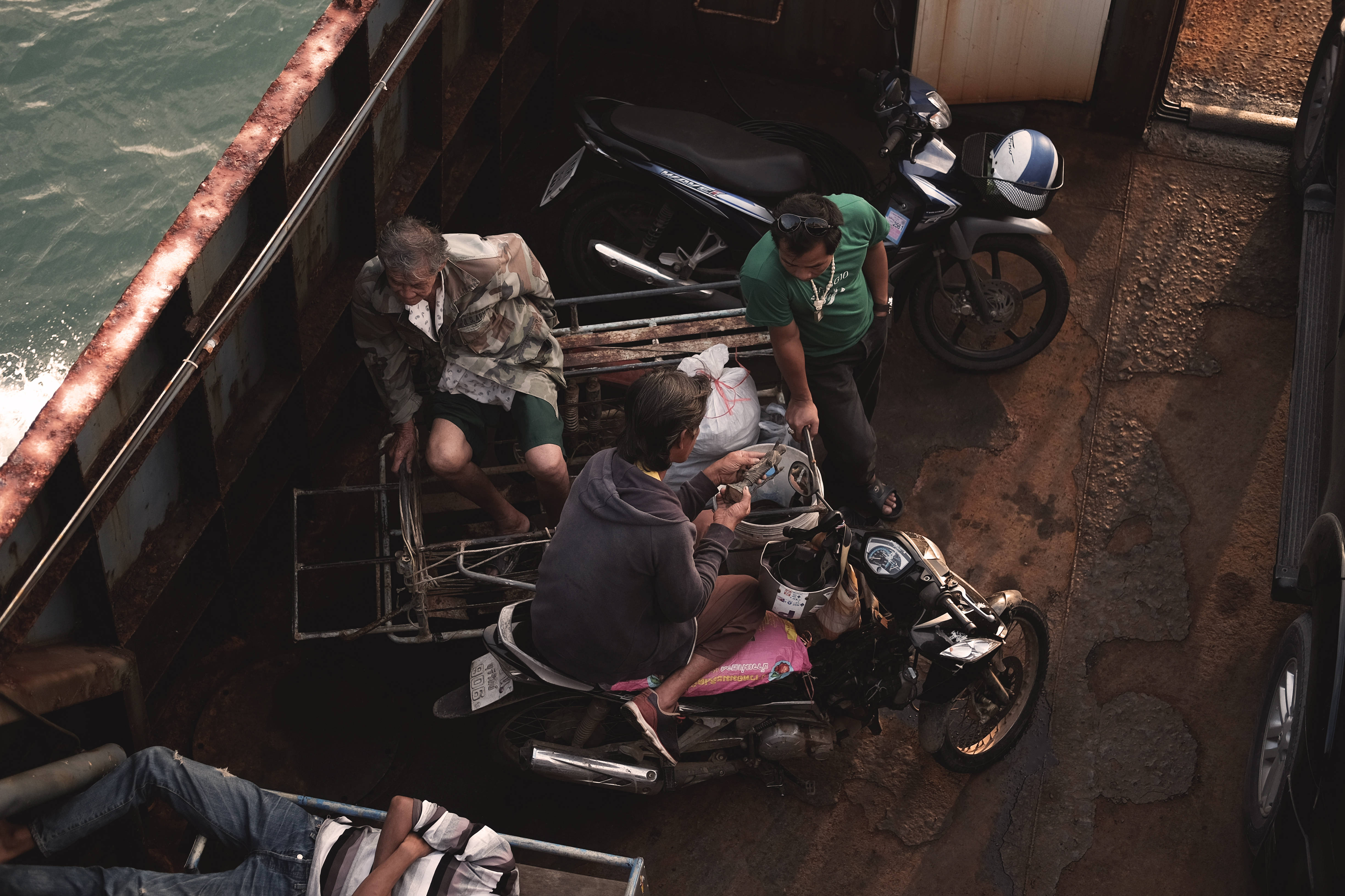 Cambodia 桌布 壁紙 — 從上方俯瞰人們將機車裝載到停泊在海濱的鏽蝕渡輪上。