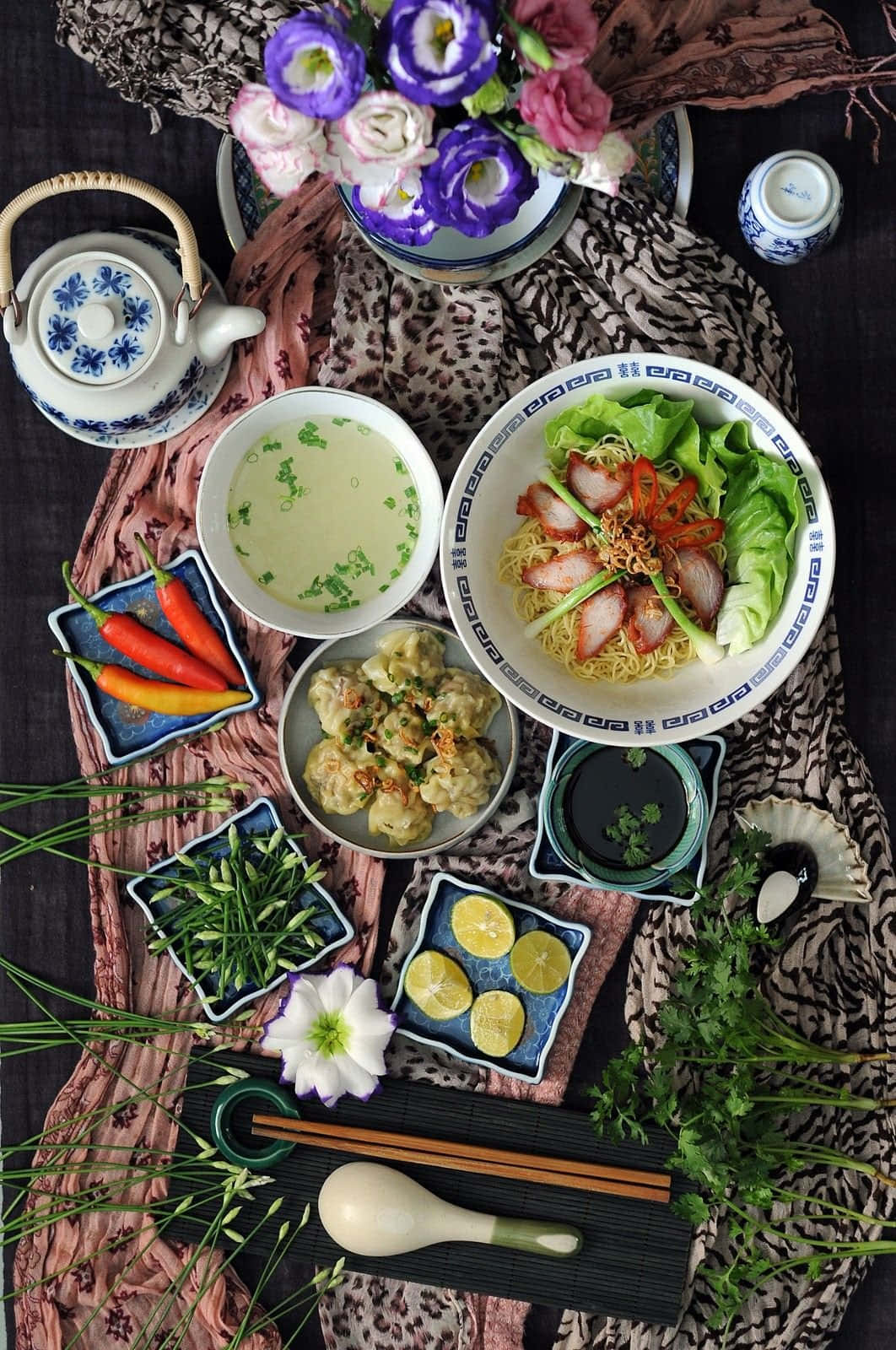 有麵條、雲吞湯和配菜的亞洲餐點，放在圖案紡織品上。 — 感恩節 iPhone 壁紙