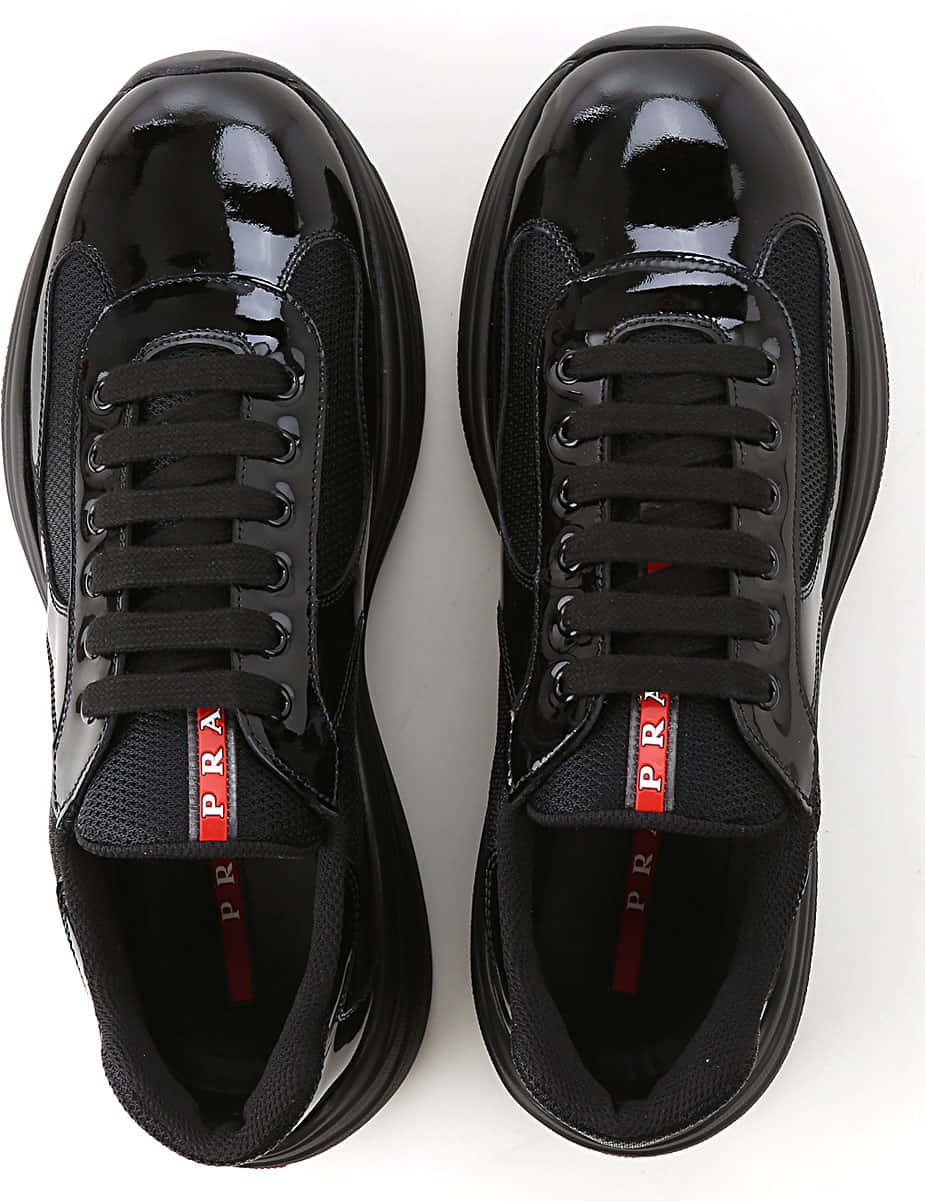 Prada 桌布 壁紙 — 從上方俯瞰光澤黑色Prada運動鞋，帶有紅色品牌標誌，背景為純白色。