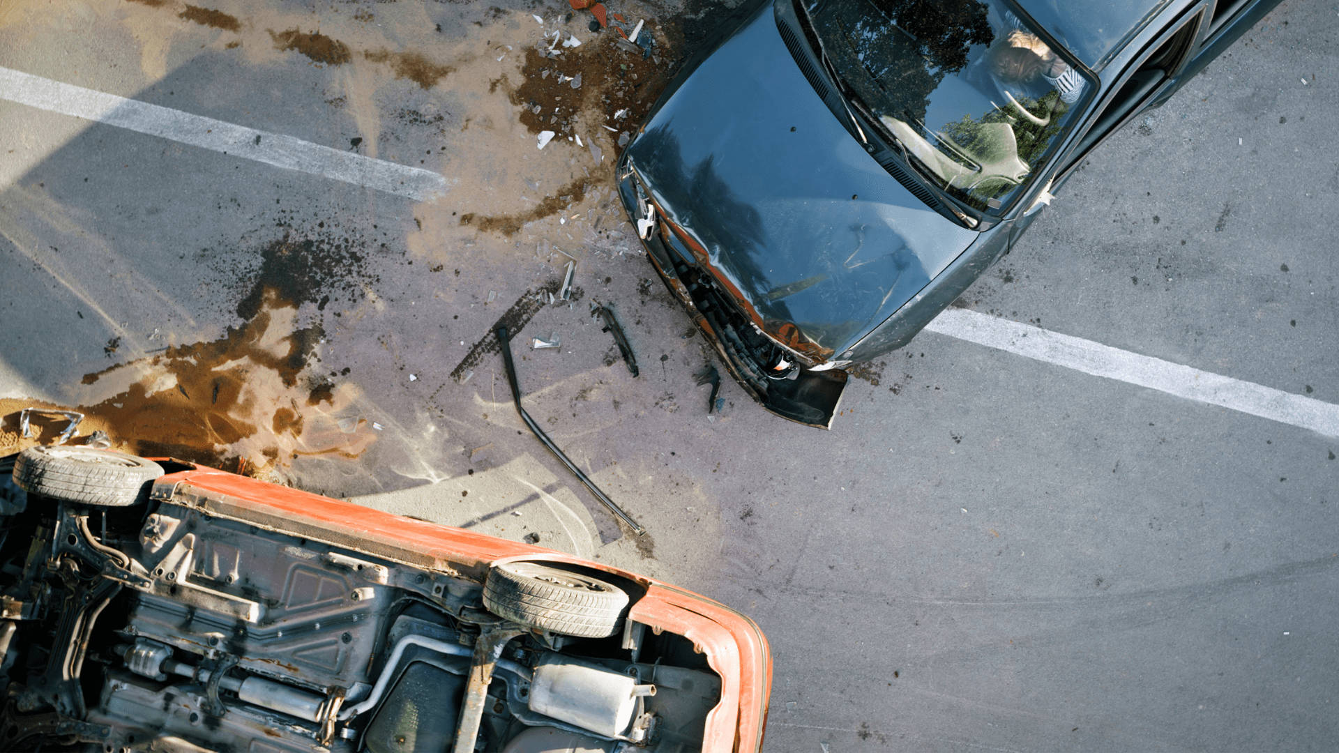車禍 桌布 壁紙 — 從上方俯瞰兩輛在陽光照射的瀝青路上碰撞後損毀的汽車，路面有灑出的液體和碎片。