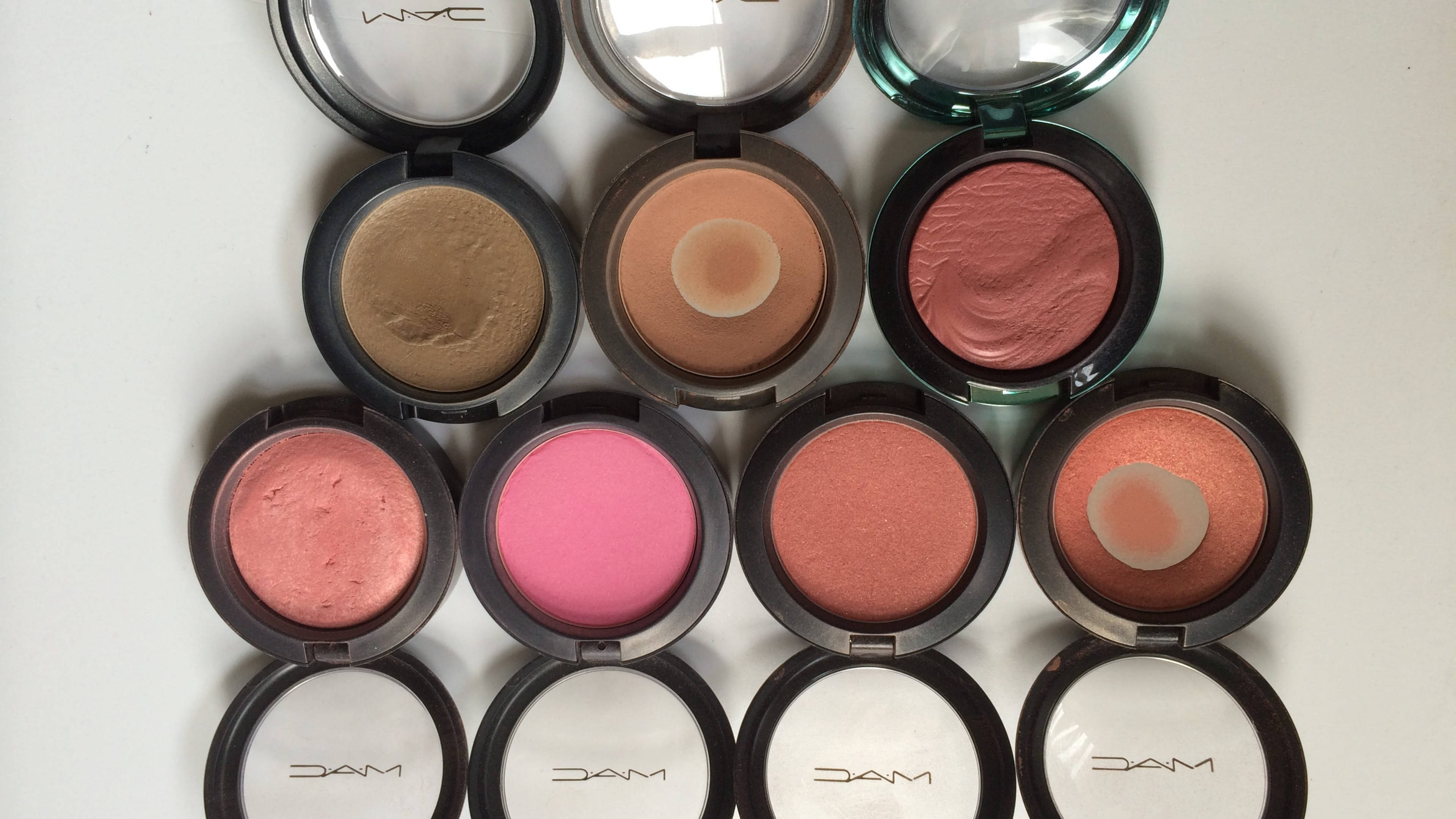 Cosmetics 桌布 壁紙 — 從上方俯瞰十個打開的MAC腮紅粉盒，整齊排列在白色表面上，展示從霧面到閃爍的各種色調。
