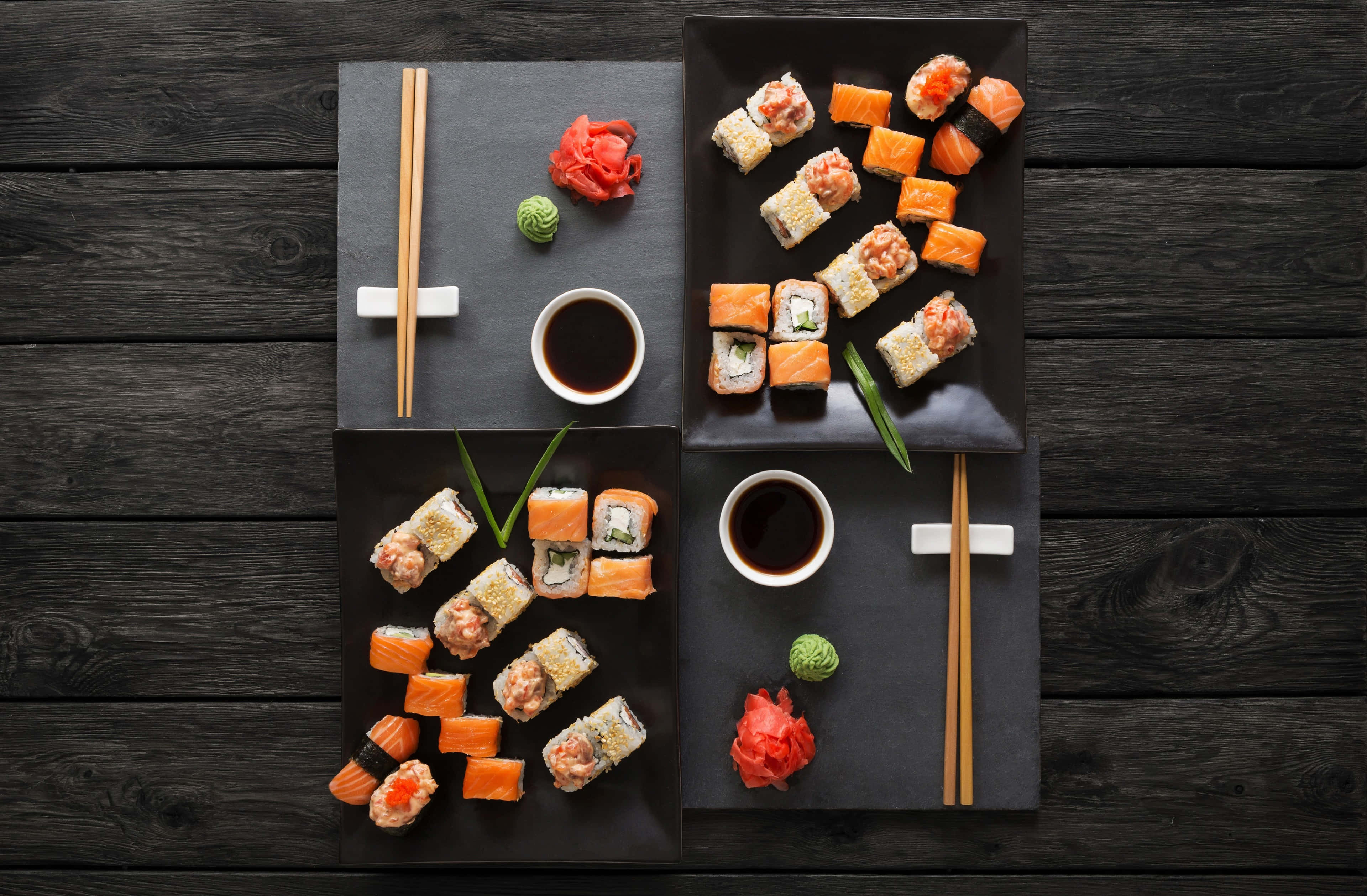 Sushi 桌布 壁紙 — 從上方俯瞰各種壽司卷和生魚片放在黑色石板盤上，搭配醬油、生薑和芥末，置於深色木桌上。