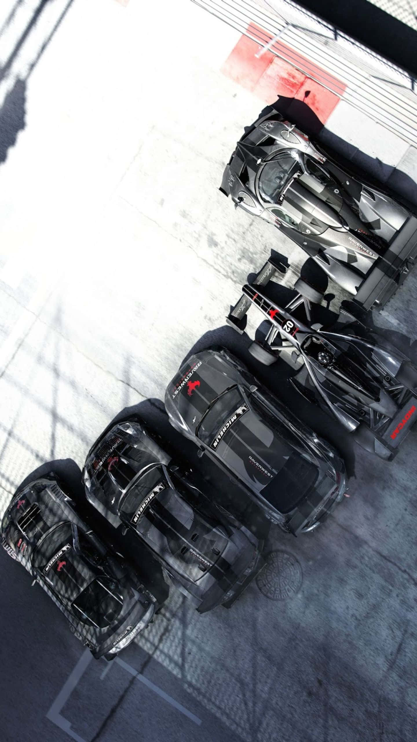 Android Grid Autosport 桌布 壁紙 — 從上方俯瞰四輛時尚黑色賽車停放在帶有紅色和白色標記的混凝土車庫中。