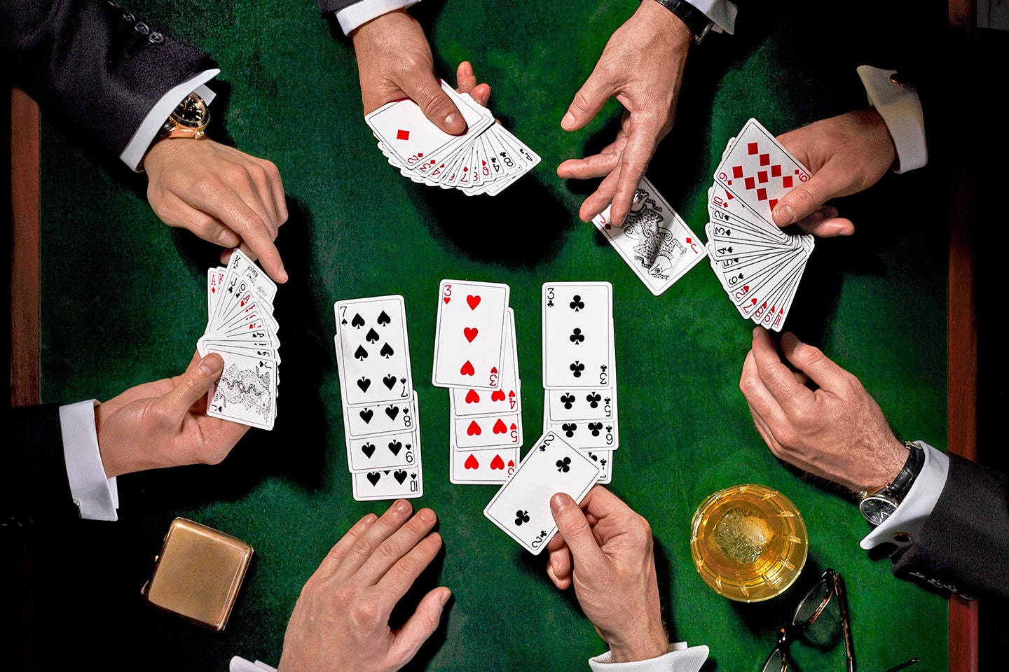 Casino 桌布 壁紙 — 從上方俯瞰多隻手在綠色氈面賭桌上發牌和持牌，旁邊有一杯威士忌和一個煙盒。