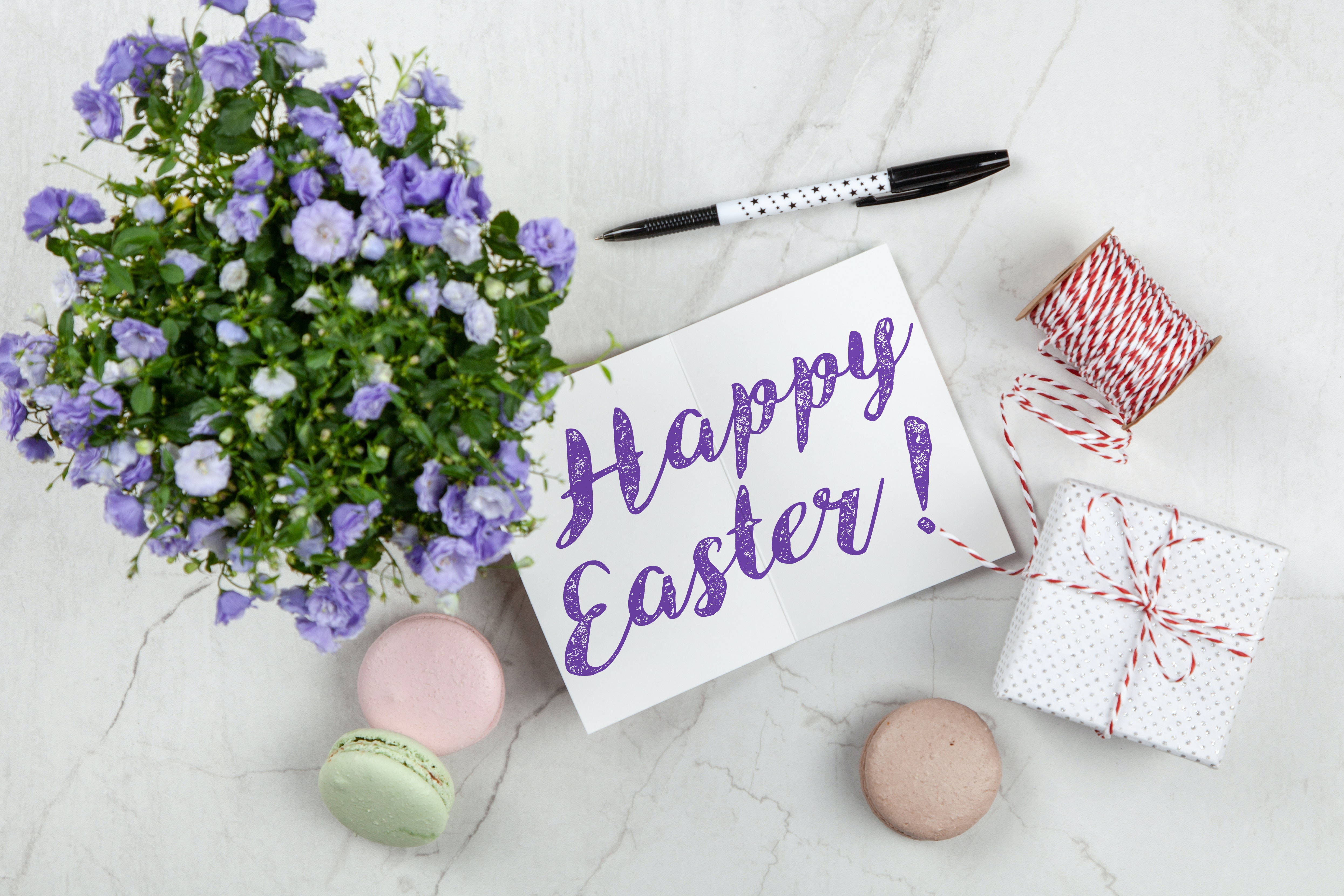Happy Easter 桌布 壁紙 — 從上方俯瞰大理石表面上的復活節主題物品，包括紫色花朵、馬卡龍、禮物和卡片。