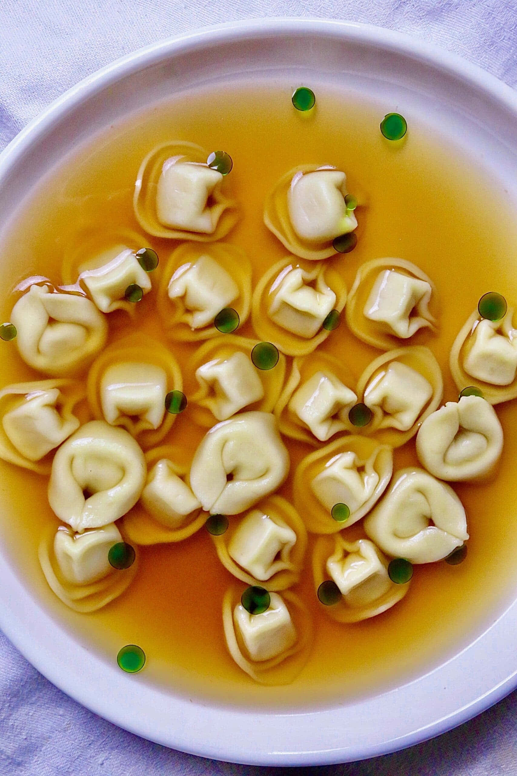 Food Photography 桌布 壁紙 — 從上方俯瞰白色碗中盛載著冒煙的義大利雲吞，配以金黃色湯汁和新鮮青豆。