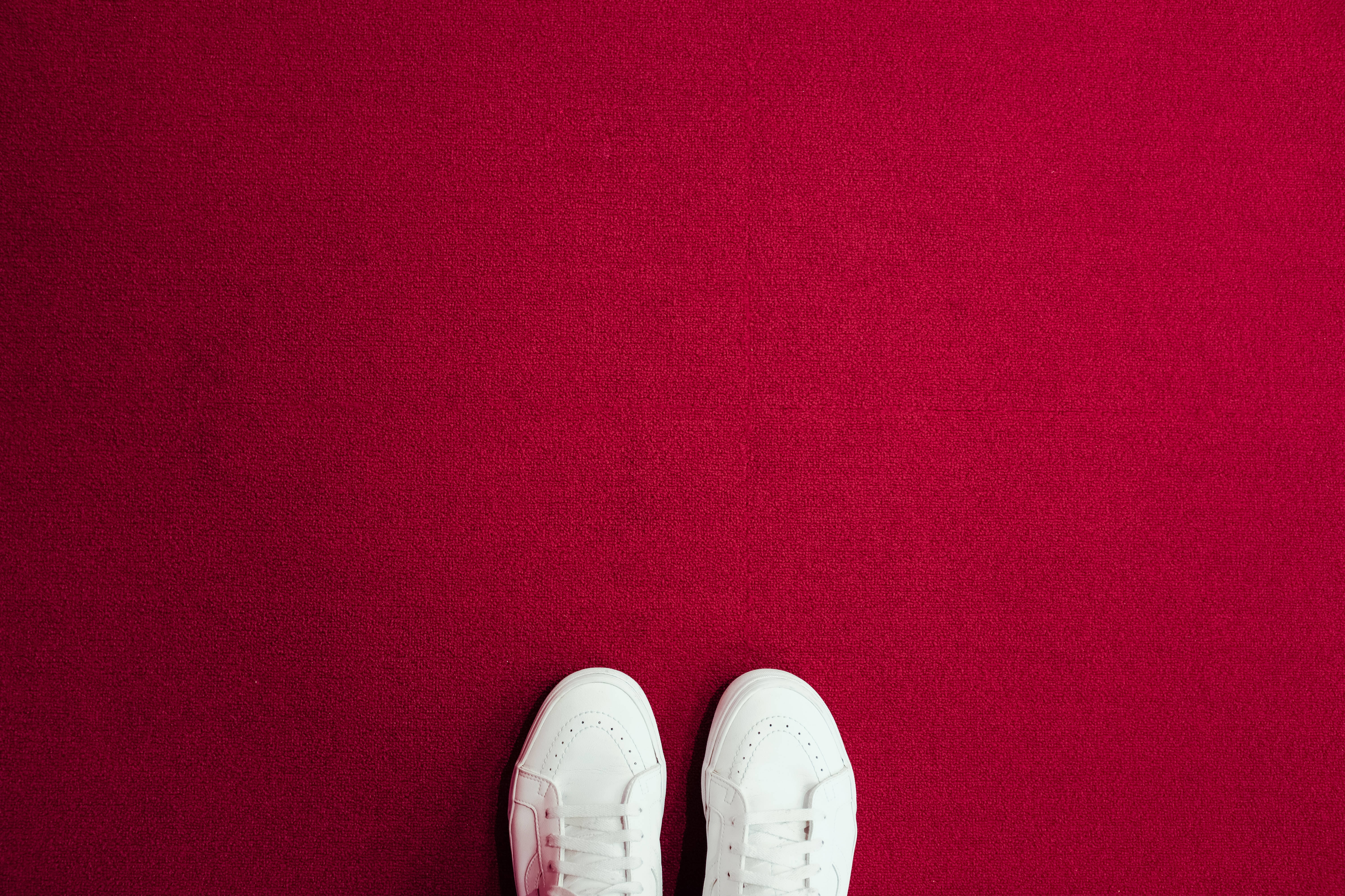 Red Carpet 桌布 壁紙 — 從上方俯瞰白色運動鞋站在質感豐富的紅色地毯上，留有充足的負空間。