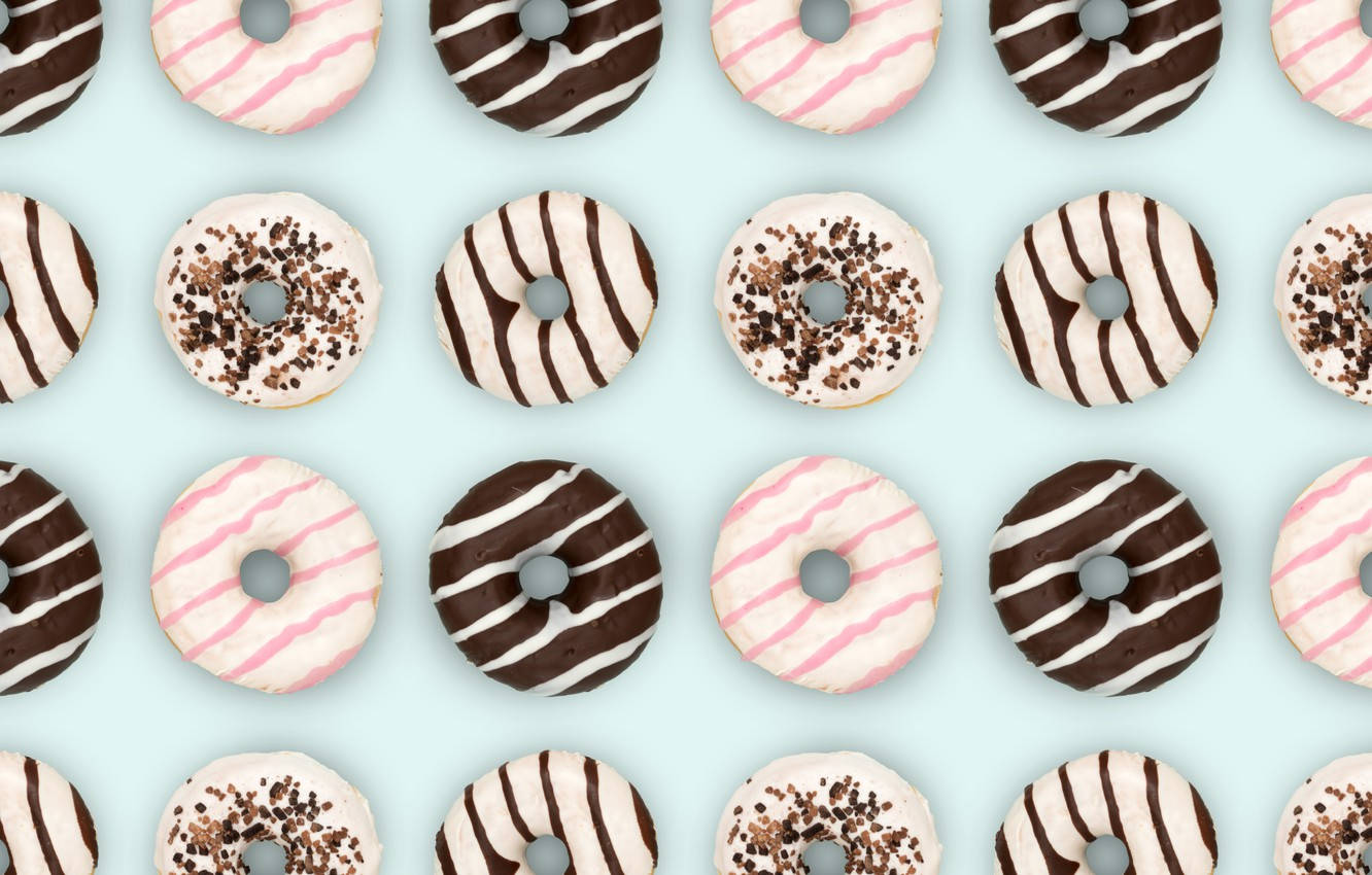 Donut 桌布 壁紙 — 從上方俯瞰的各種甜甜圈網格，帶有粉紅色條紋、巧克力淋面和彩針，背景為粉藍色。