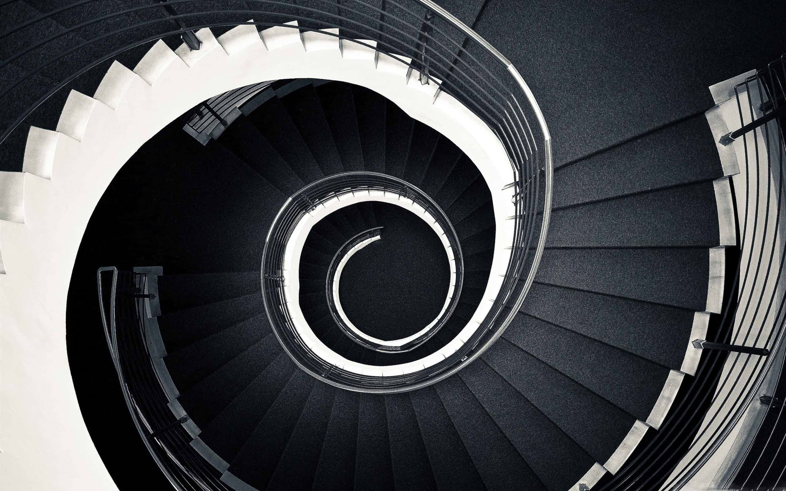 stairs 桌布 壁紙 — 從上方俯瞰的戲劇性螺旋樓梯，黑白對比強烈，營造出催眠般的漩渦效果。