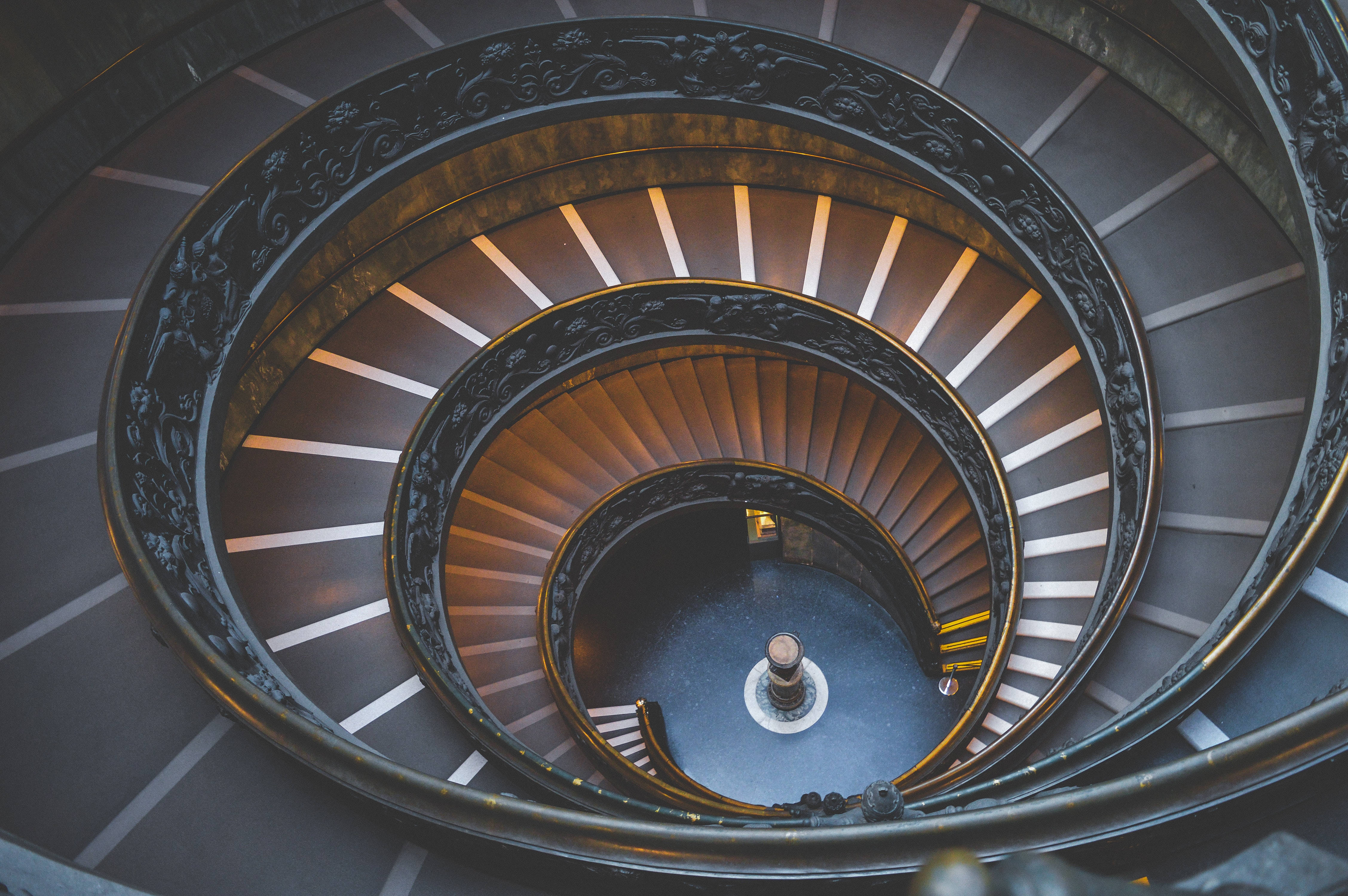 Staircase 桌布 壁紙 — 從上方俯瞰的戲劇性視角，展示一座宏偉華麗的螺旋樓梯，配有深色鐵製欄杆和溫暖的木質台階。