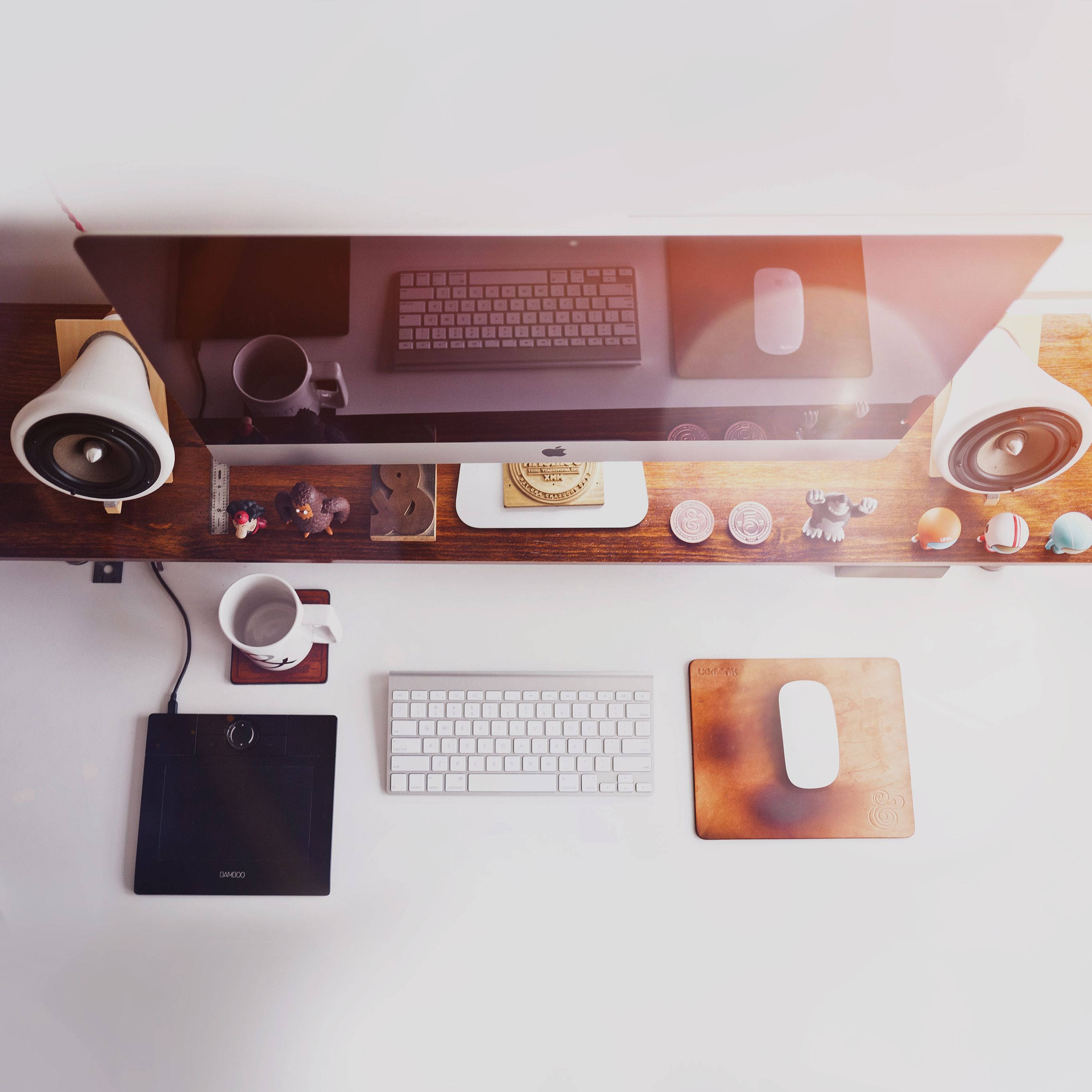 Desktop Computer 桌布 壁紙 — 從上方俯瞰的簡約白色書桌，配備雙鍵盤、滑鼠墊和顯示器，兩側有揚聲器和小型人偶。